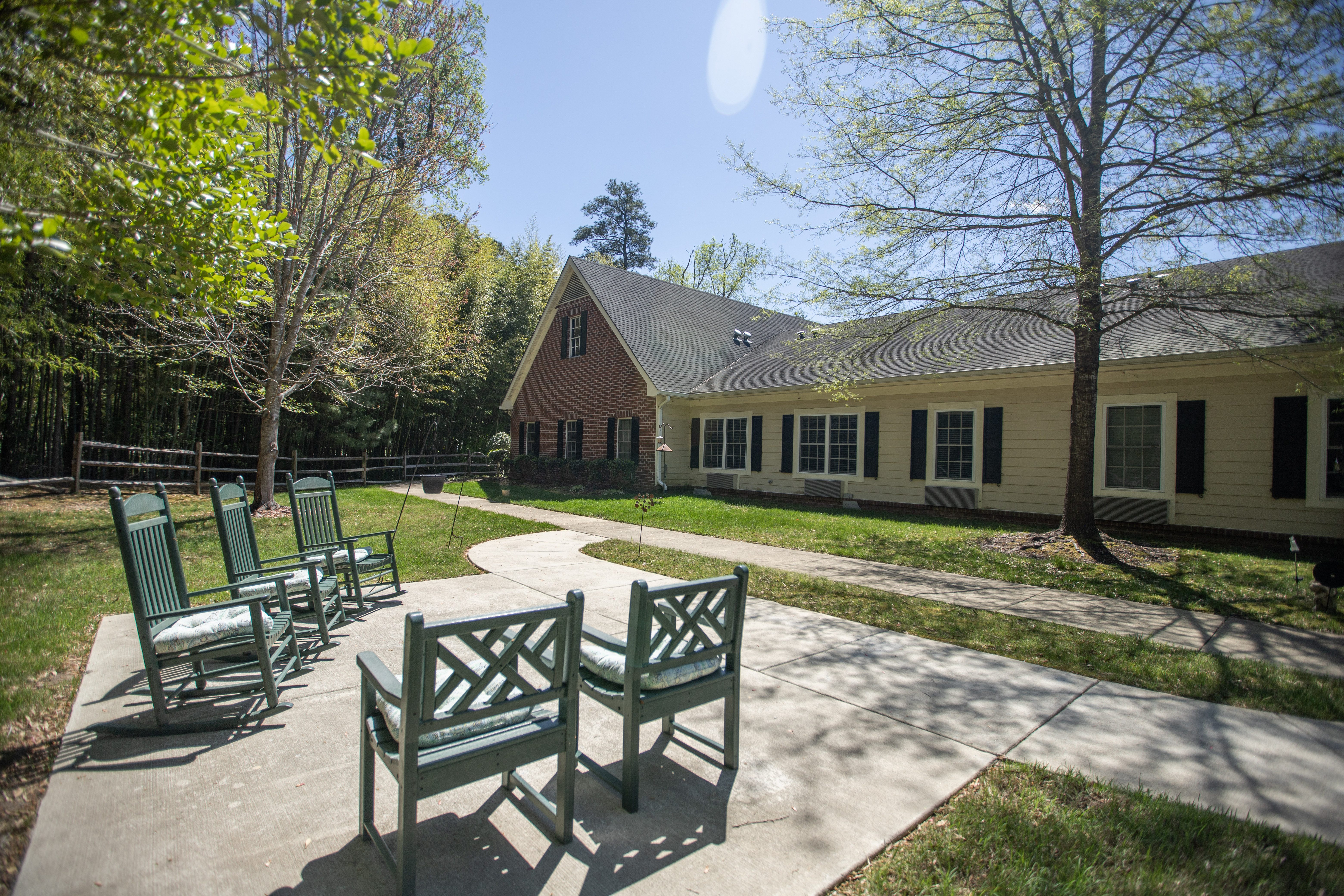 A sunny day at a park with a bench and a building in the background.at Spring Arbor of Williamsburg, Virginia