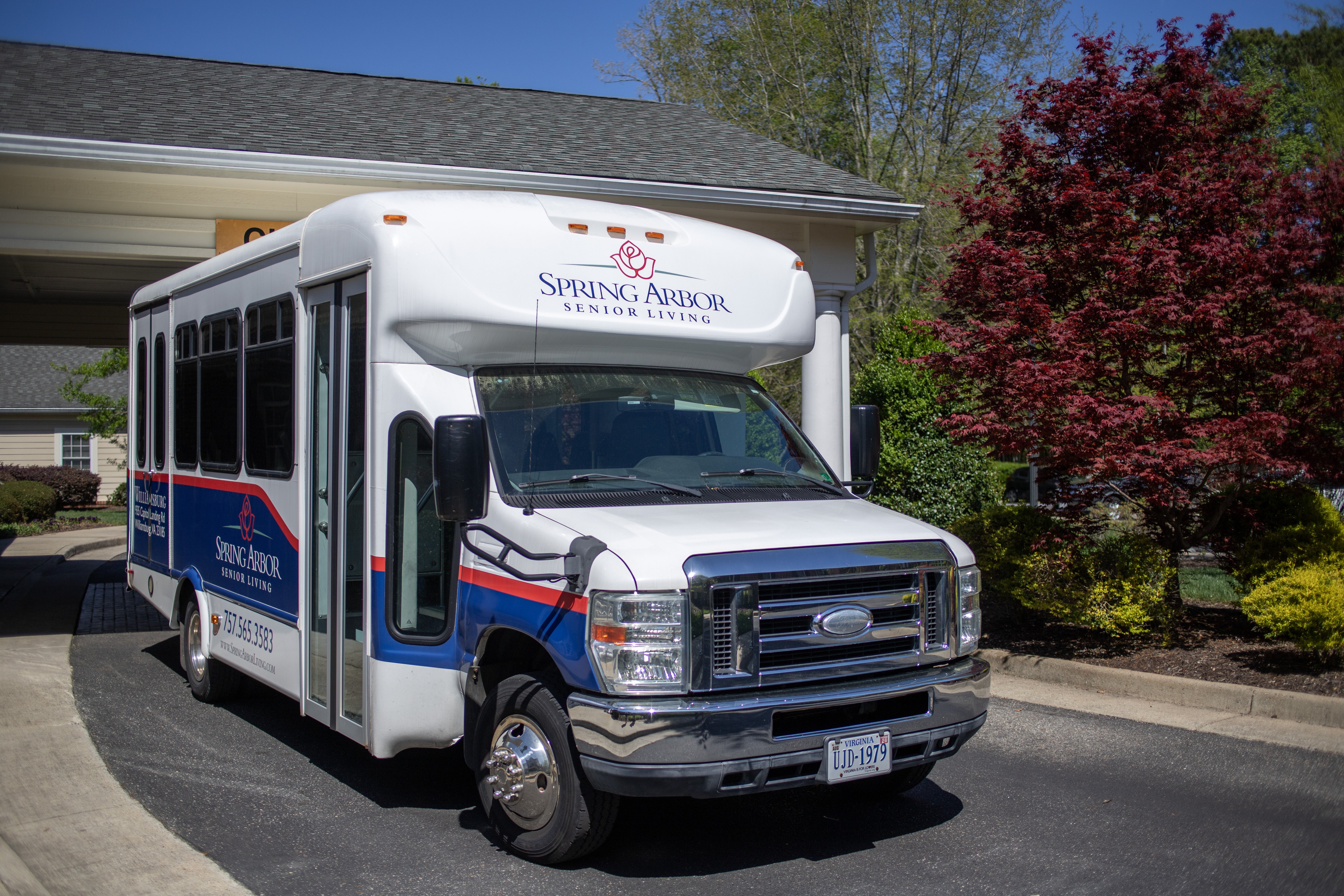 A white bus with blue and red stripes is parked in front of a building.at Spring Arbor of Williamsburg, Virginia, 23185