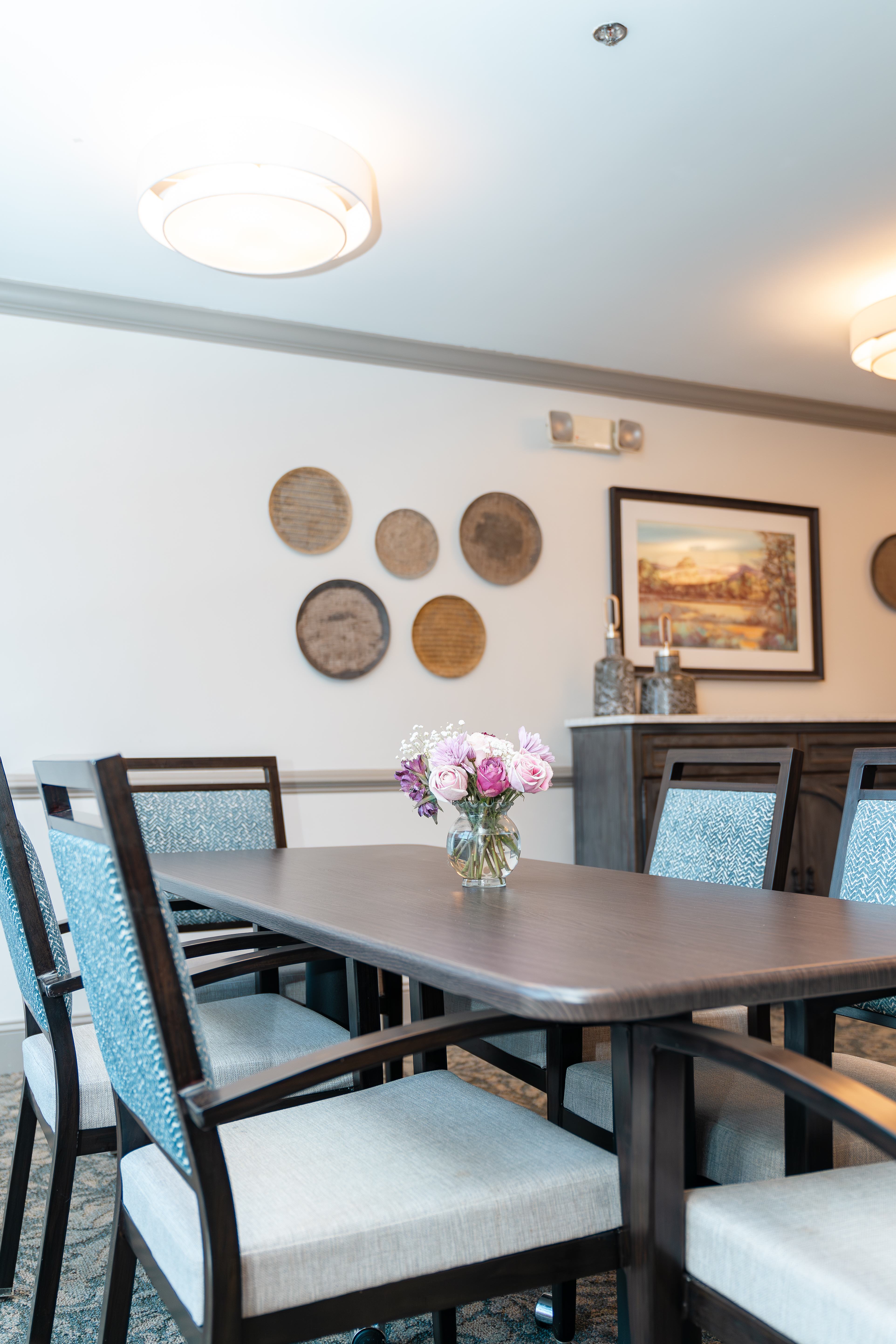 A dining table with chairs and a vase of flowers on it at Spring Arbor of Apex in Apex, NC