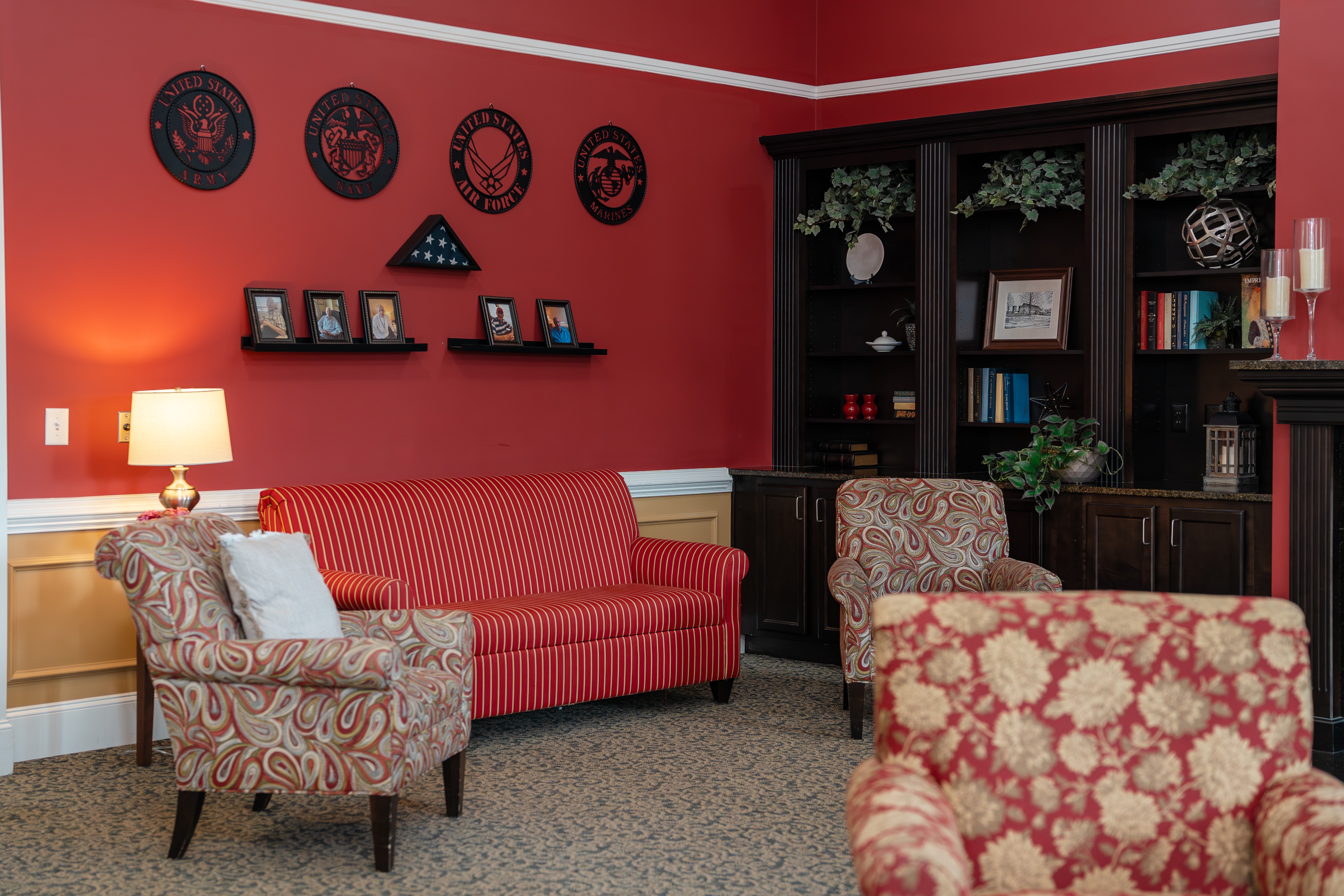 A living room with a red couch, two chairs, and a bookcase at Spring Arbor of Cary in Cary, NC