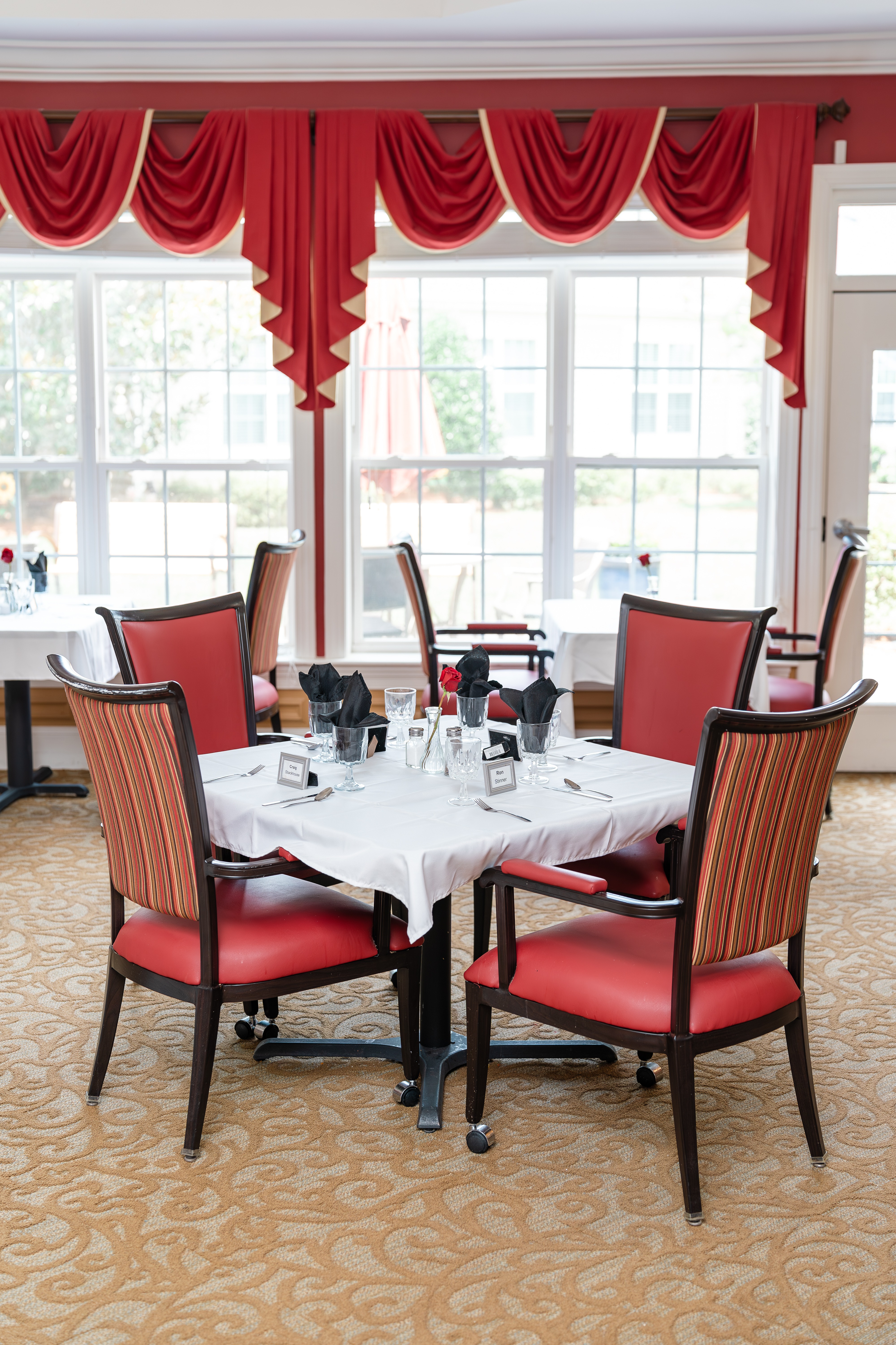 Dining room with red chairs and a white tablecloth is set for a meal  at Spring Arbor of Cary in Cary, NC