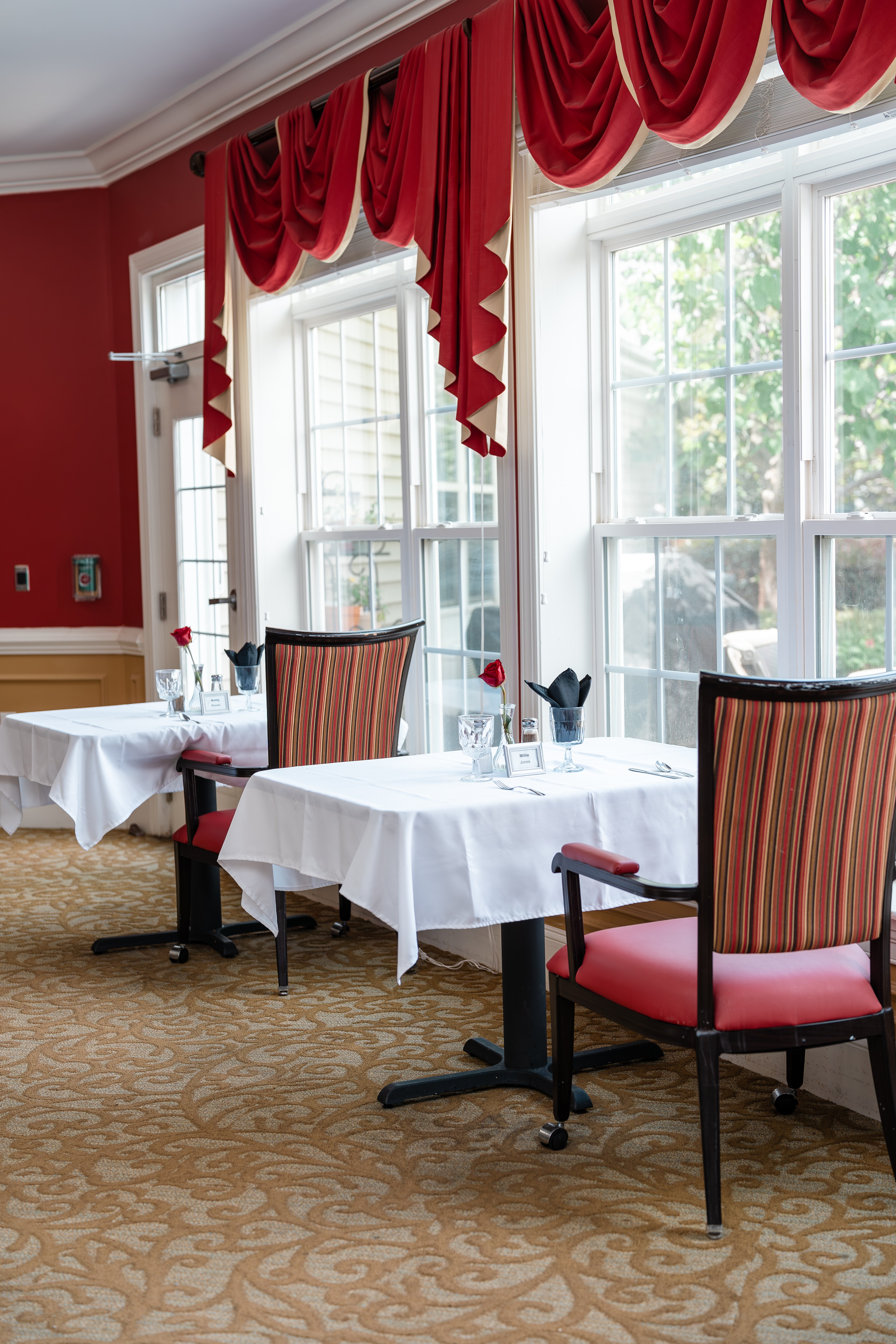 A dining room with red chairs and white tablecloths at Spring Arbor of Cary in Cary, NC