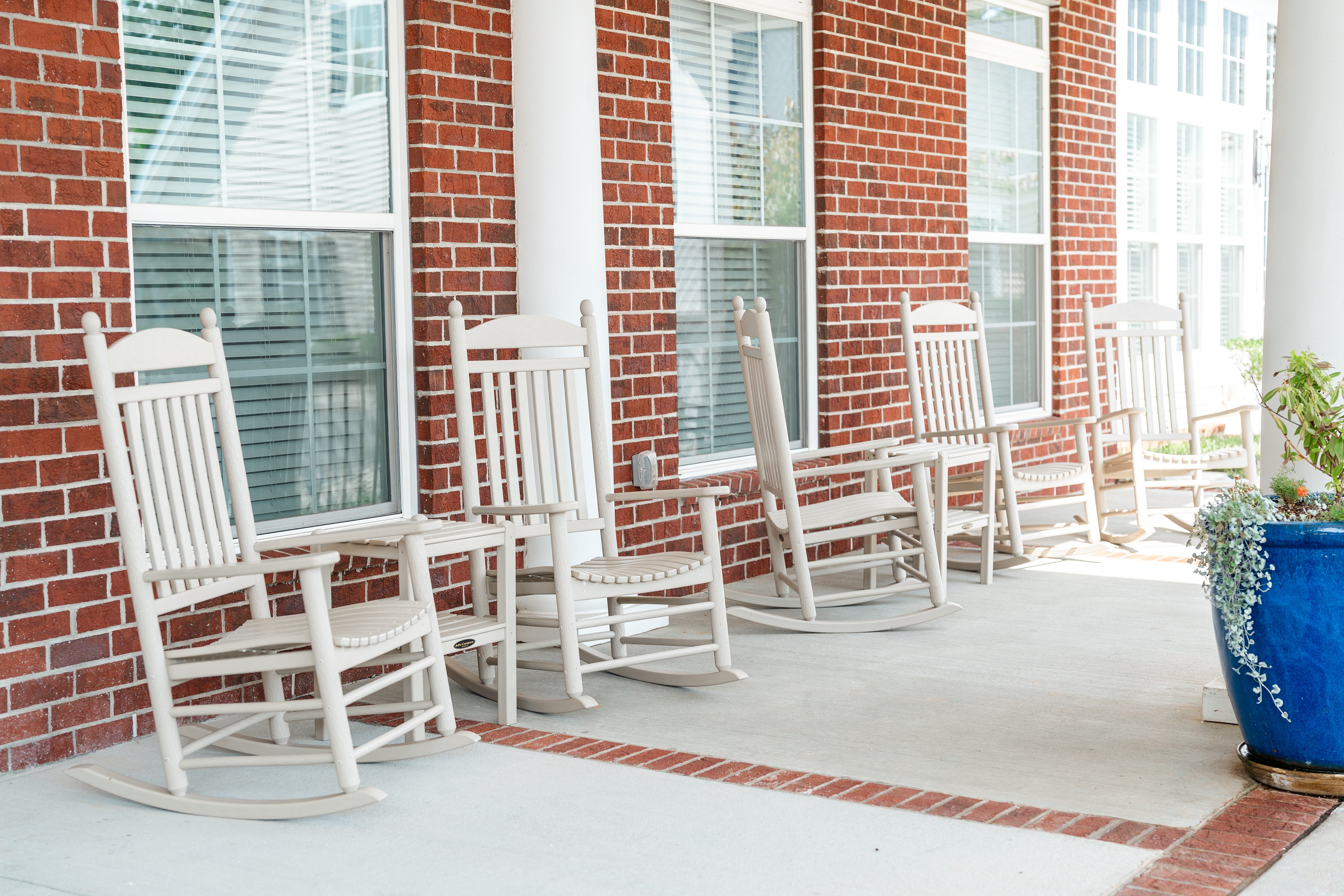 A row of white rocking chairs are lined up on a porch at Spring Arbor of Cary in Cary, NC