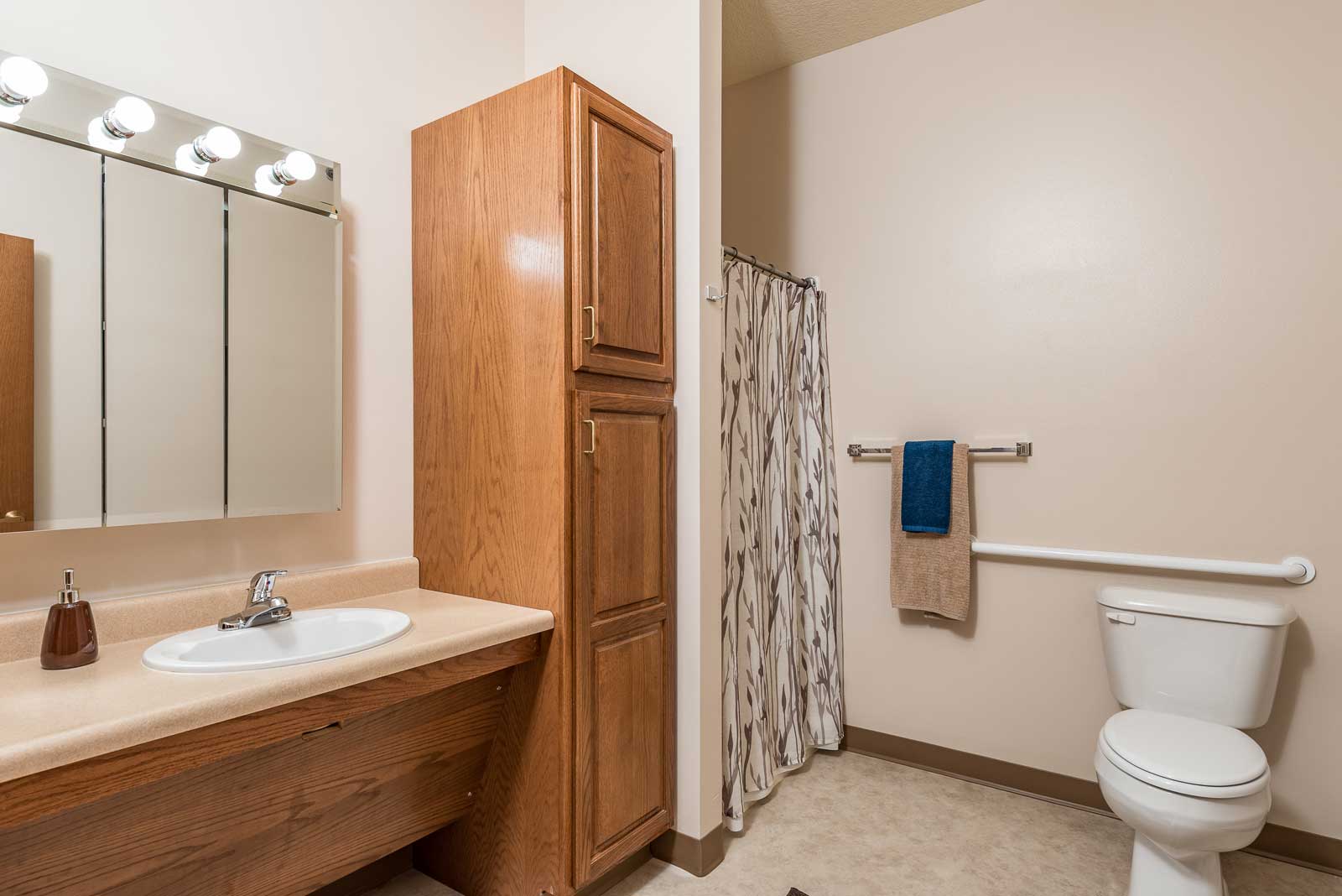 A bathroom with a toilet, sink, and wooden cabinet.at Windsor Manor Webster City, Iowa