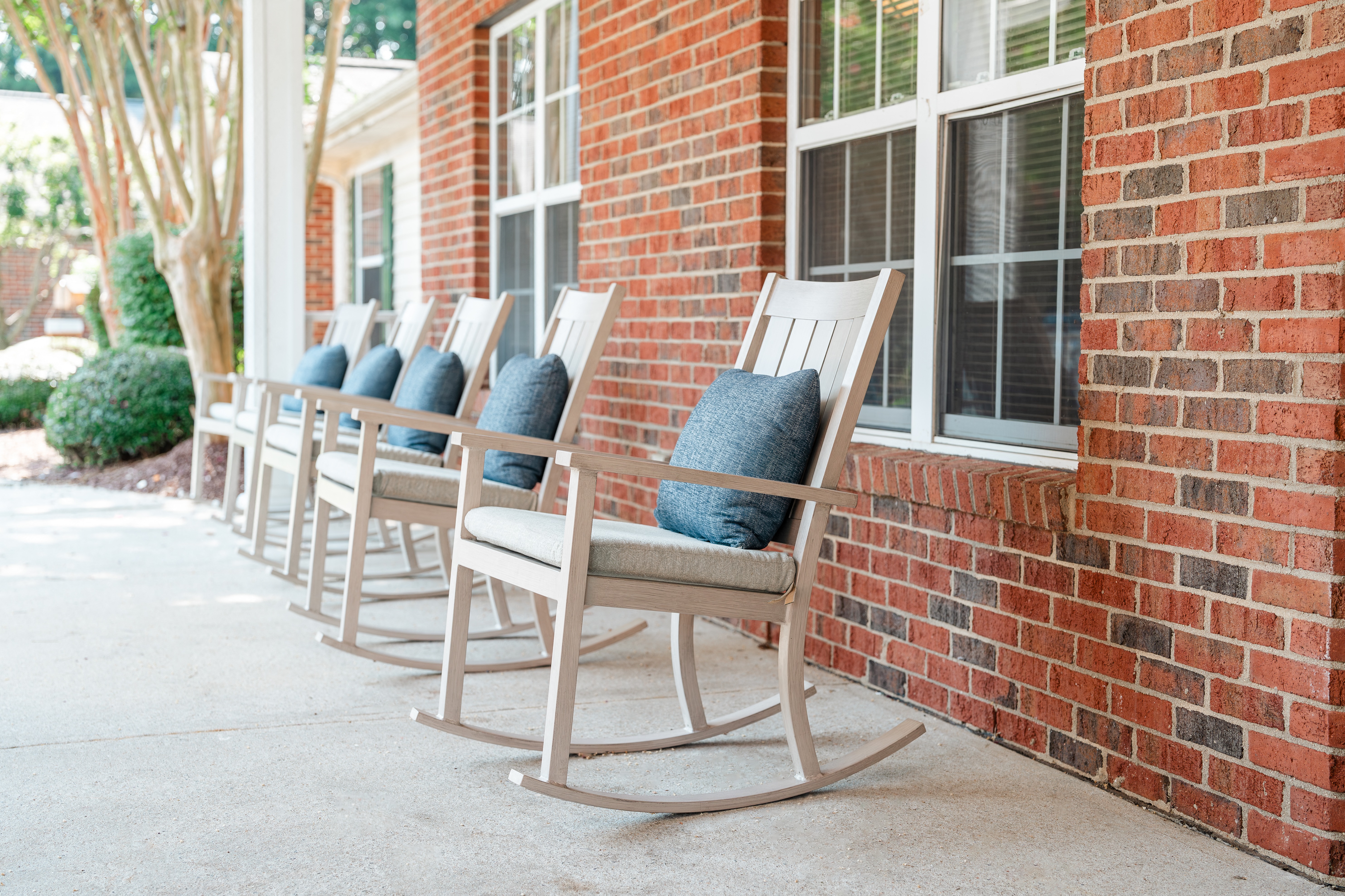 Row of rocking chairs outside of a brick building at Spring Arbor of Apex