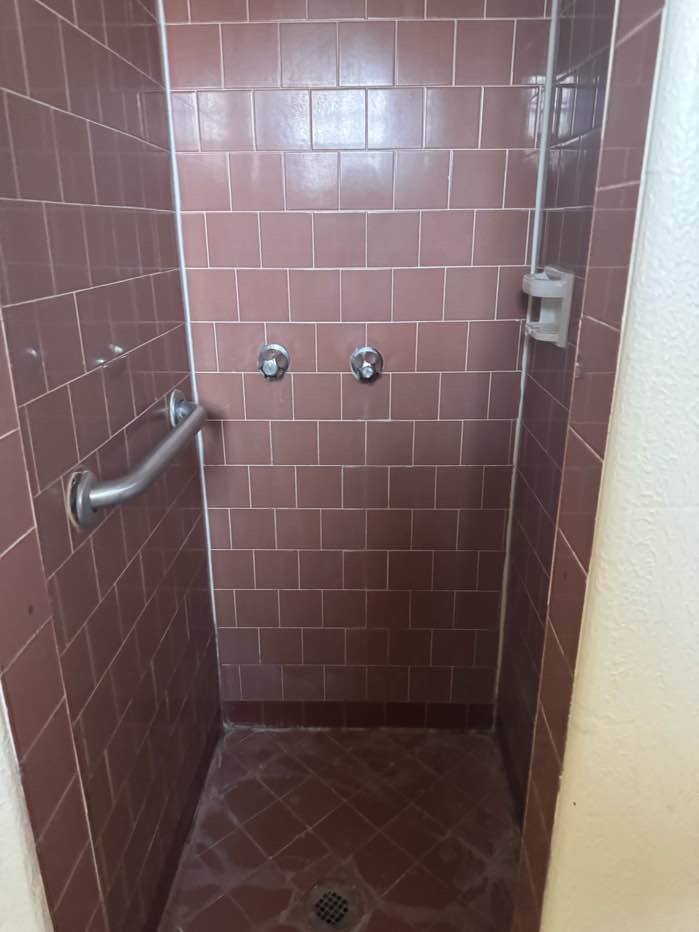 A small, dark brown tiled shower stall with a grab bar on the side.