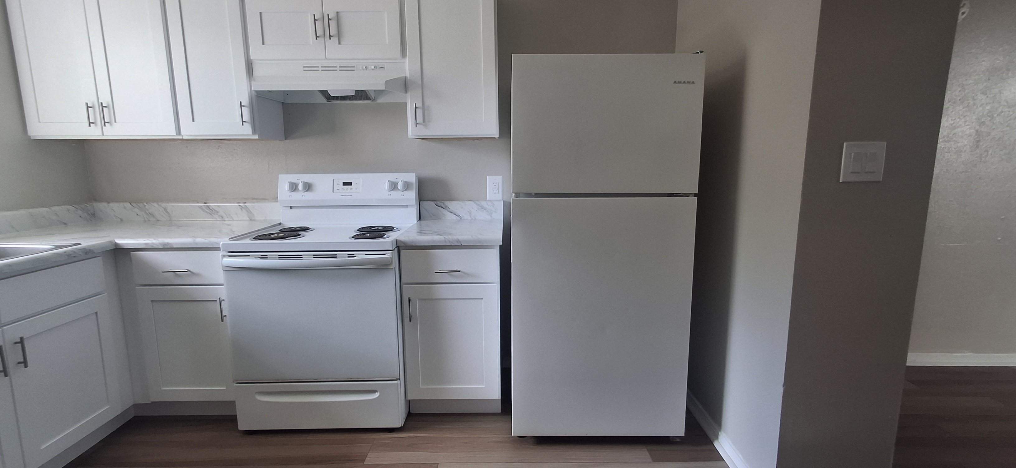 A white fridge stands in a kitchen next to a white stove.