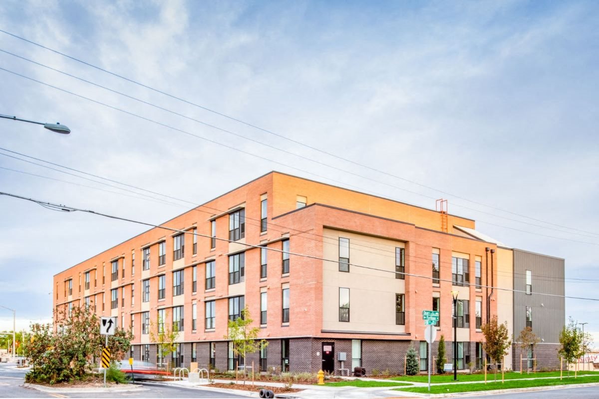 Exterior shot facing south, 3 stories of salmon covered bricks, bottom story grey bricks, windows, and some peach stucco on top 2 floors facing east
