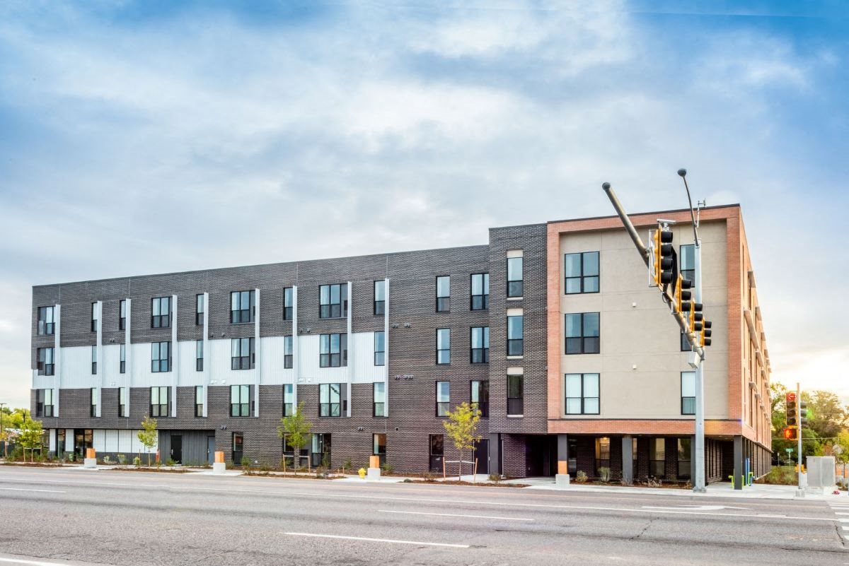 Exterior shot of Peoria Crossing facing west, grey bricks on top half, windows, and white siding and salmon colored brick on the south end of building