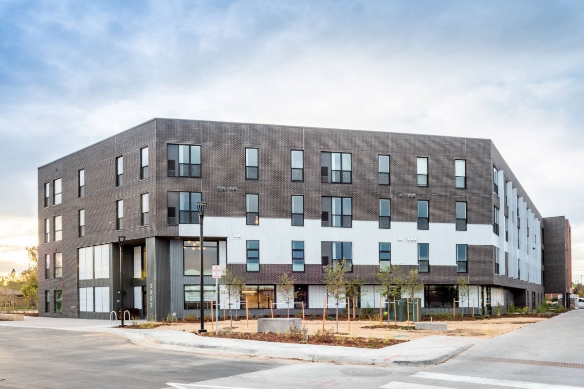 Exterior shot of Peoria Crossing Apartments, grey bricks on top half, windows, and white siding on lower half