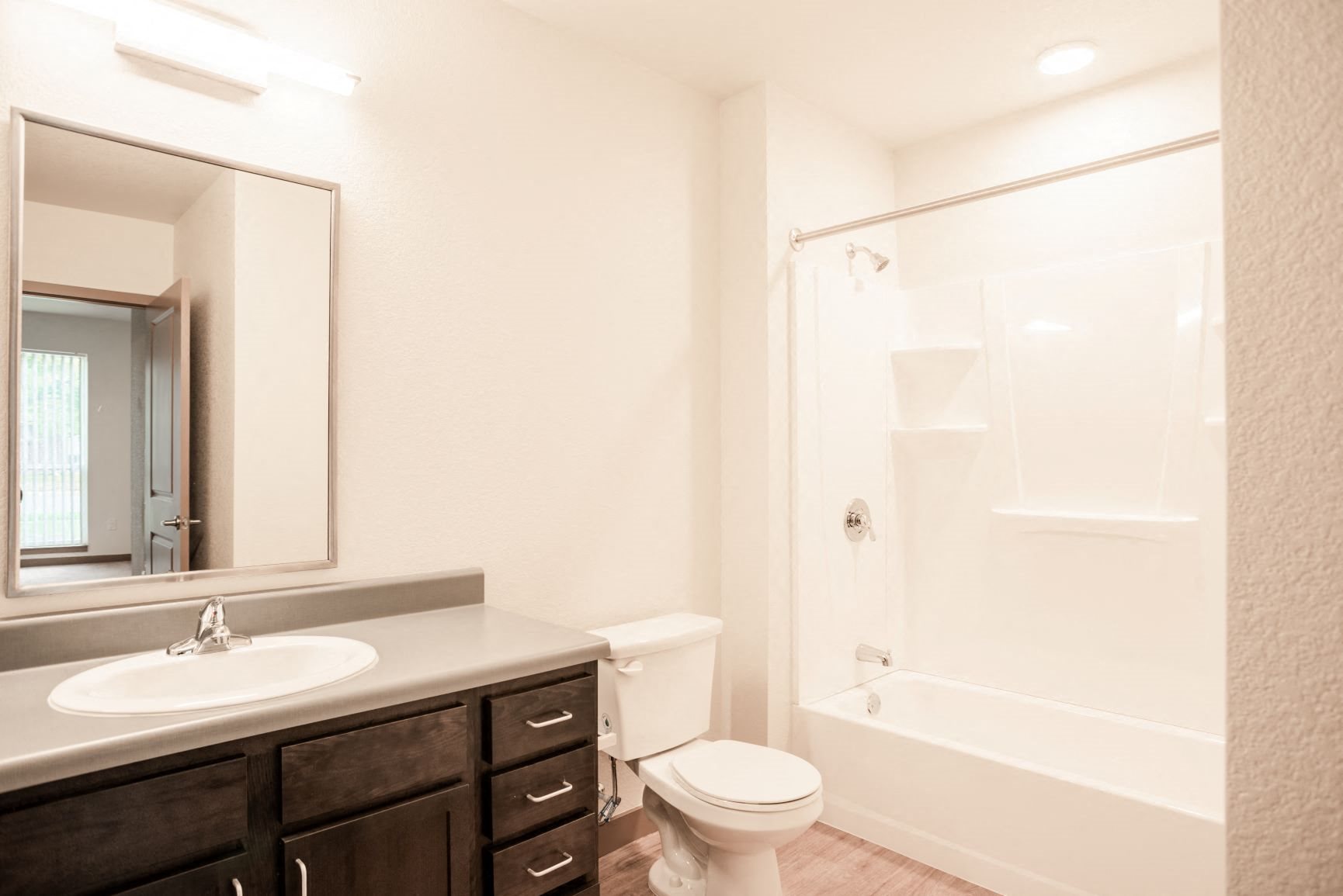 Bathroom with bathtub style shower, pot light over bath tub, toilet, sink, and dark brown cabinets and grey counter top