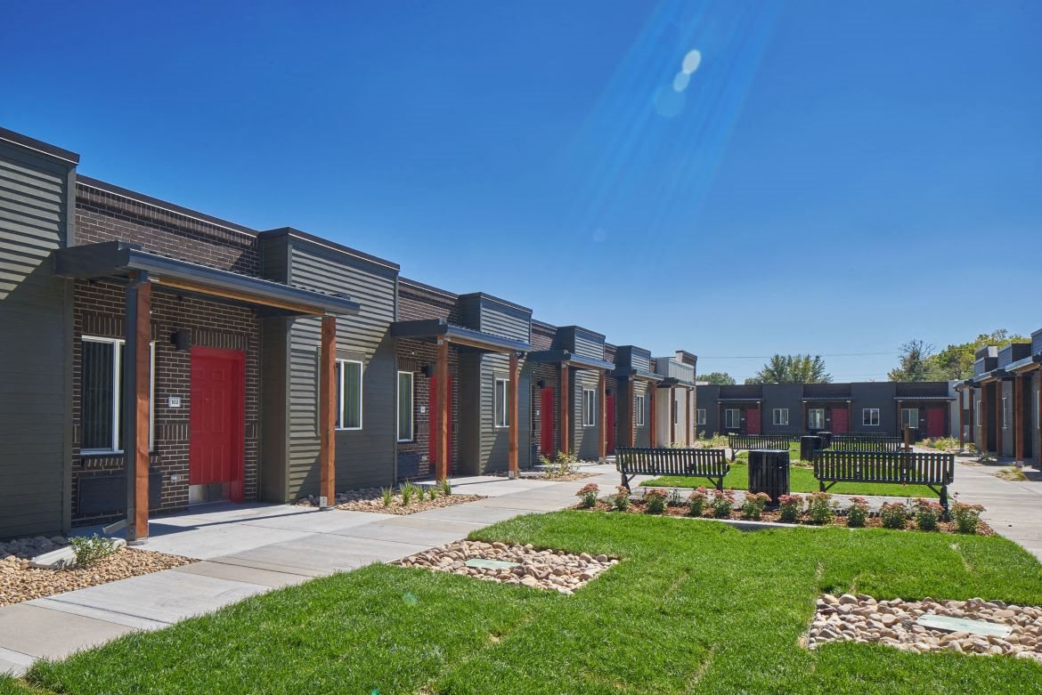 Exterior view of VWC3, row home style units made up of dark brown brick and dark green siding, red doors with awnings and courtyard