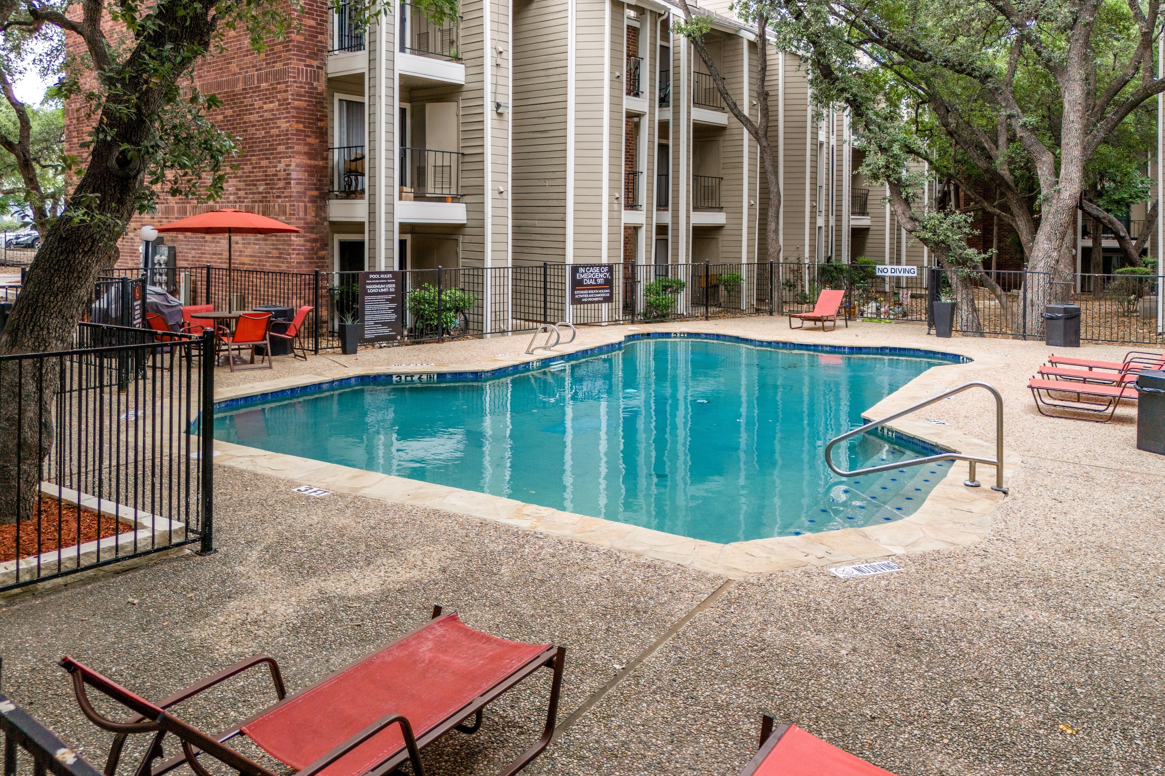A small pool surrounded by a black fence and red sunshades.