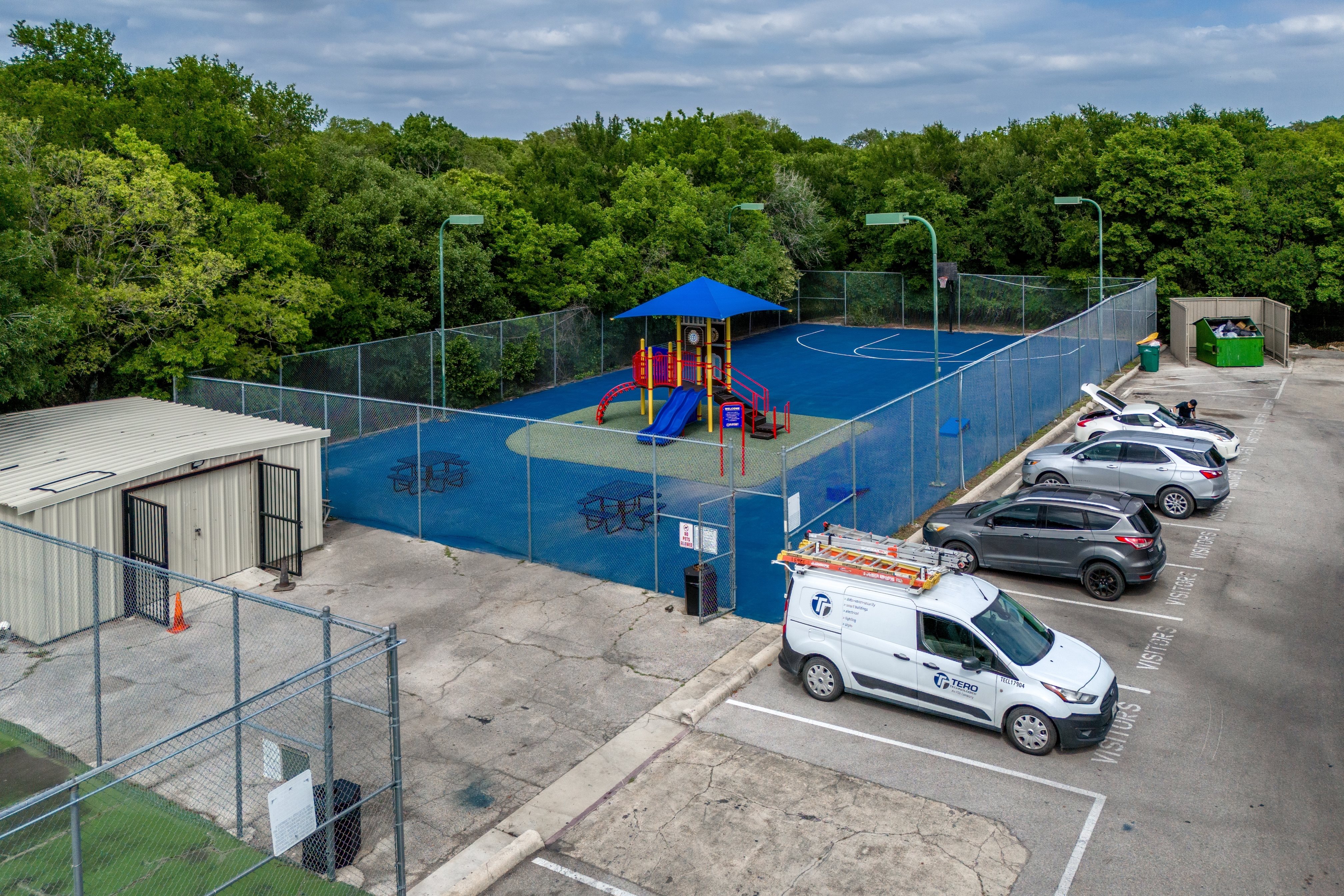 A playground with a blue fence and a white van parked in front of it.