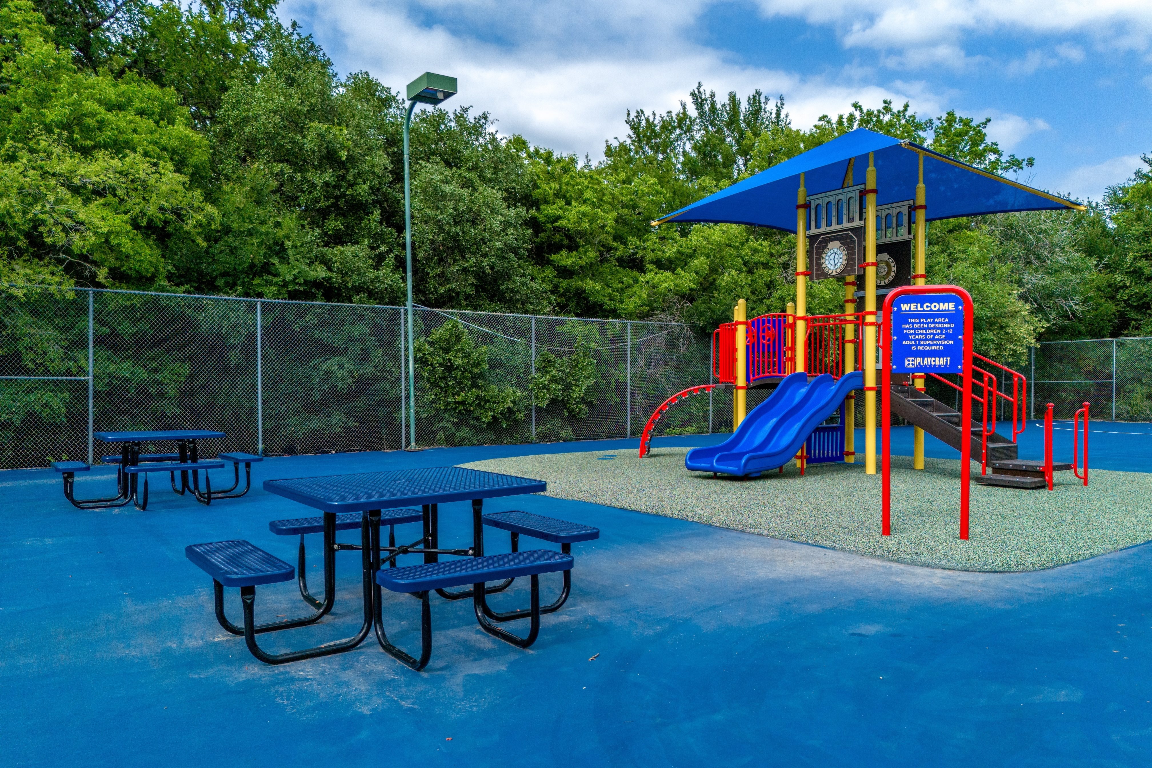 A playground with a blue slide and picnic tables.