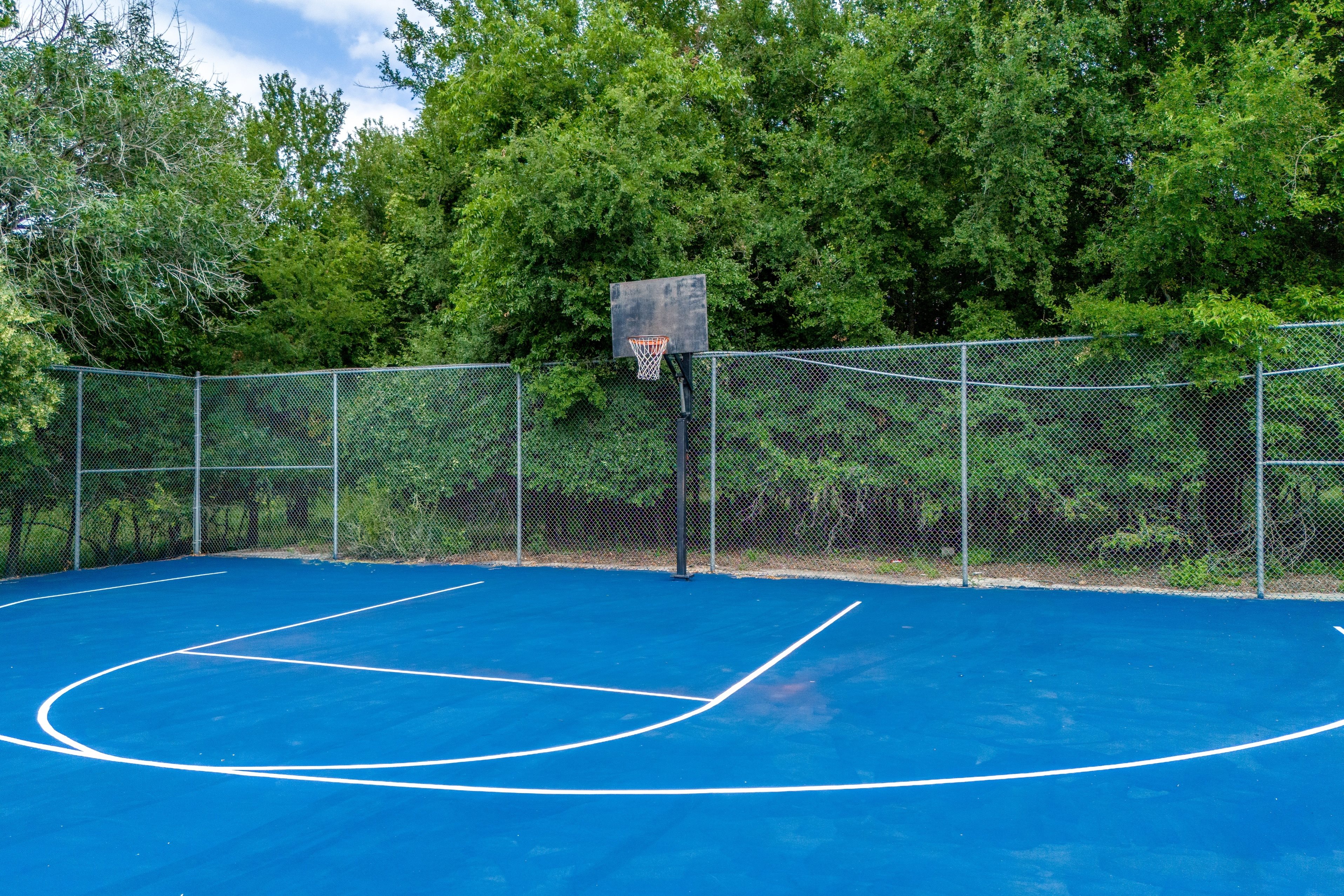 A basketball court surrounded by a fence with trees in the background.