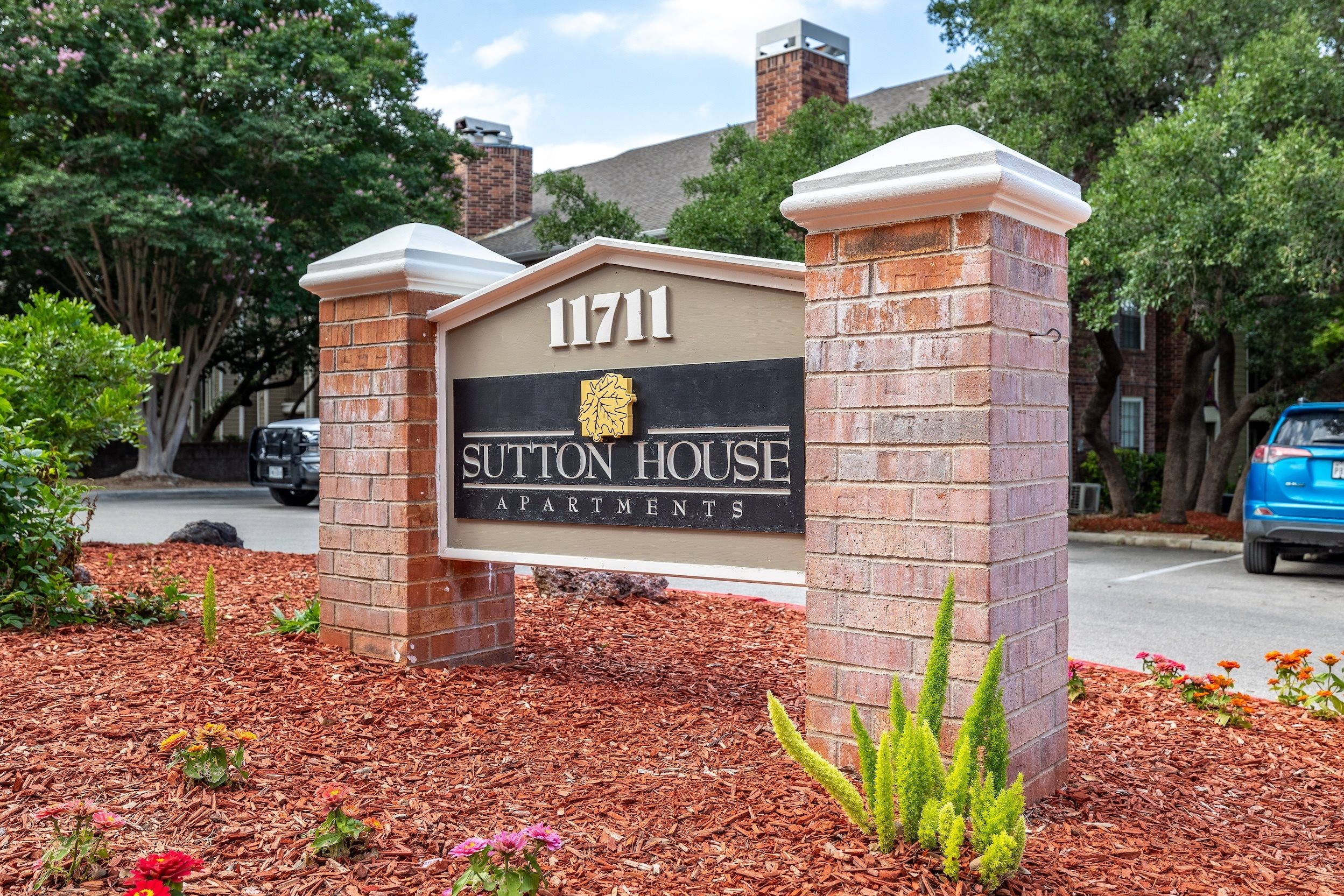 A sign for Sutton House Apartments is displayed in front of a brick wall.
