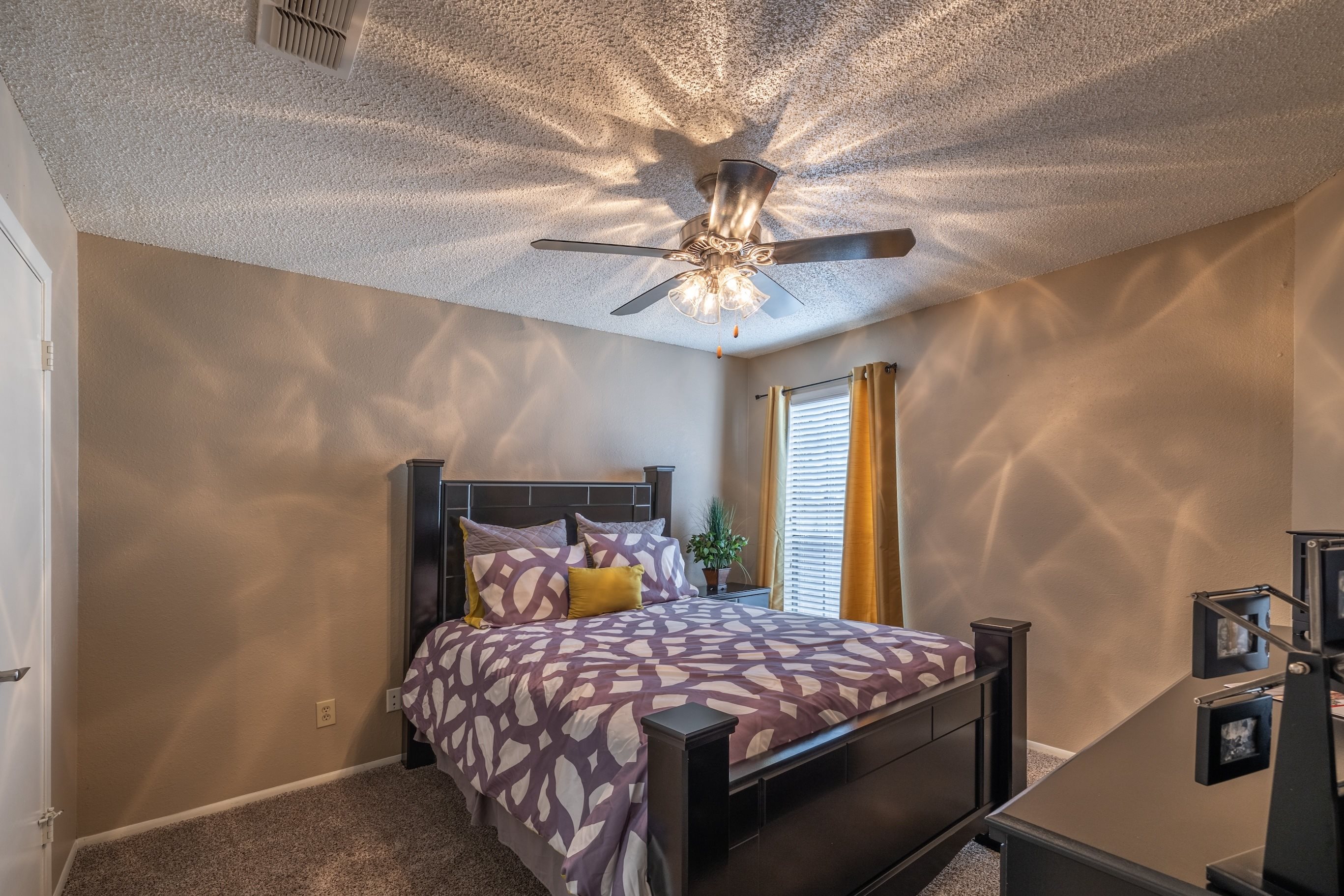 A bedroom with a bed, a ceiling fan, and a window with blinds.