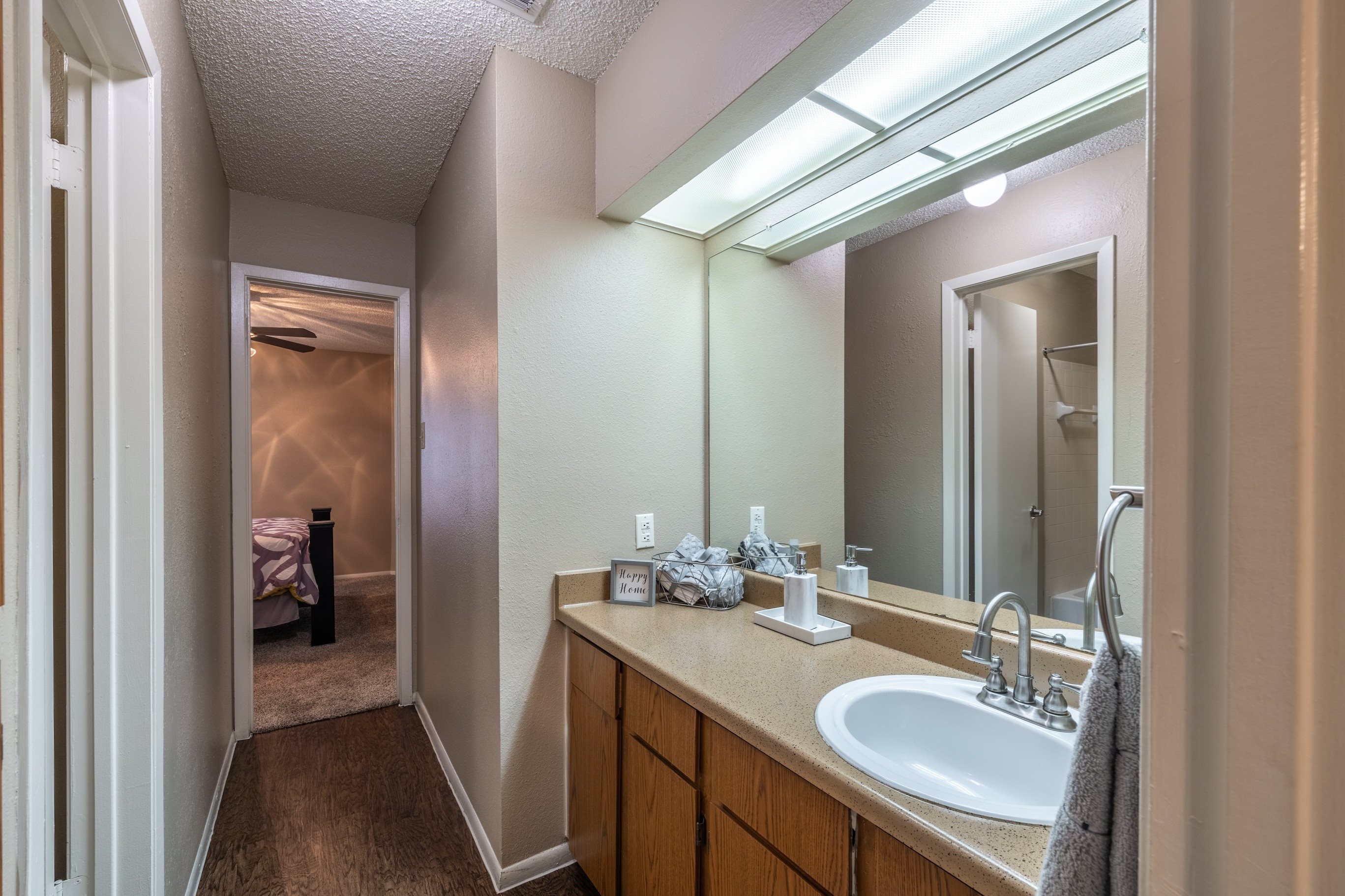 A bathroom with a sink, mirror, and a bed in the background.