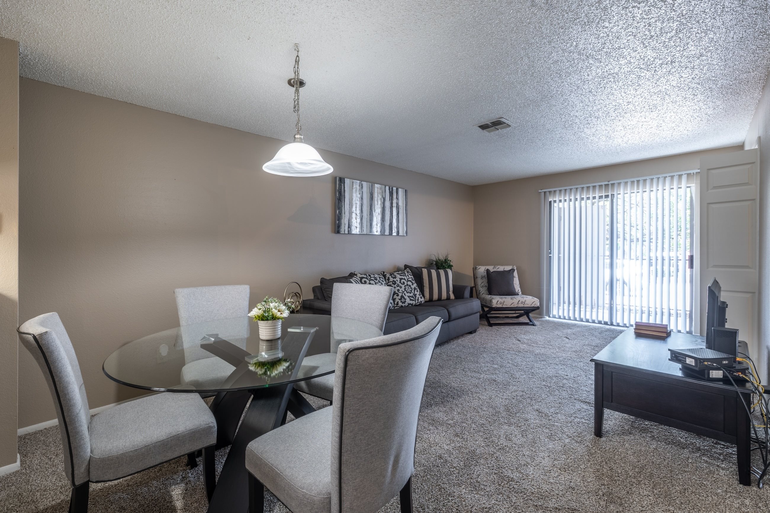 A living room with a glass table and grey chairs.