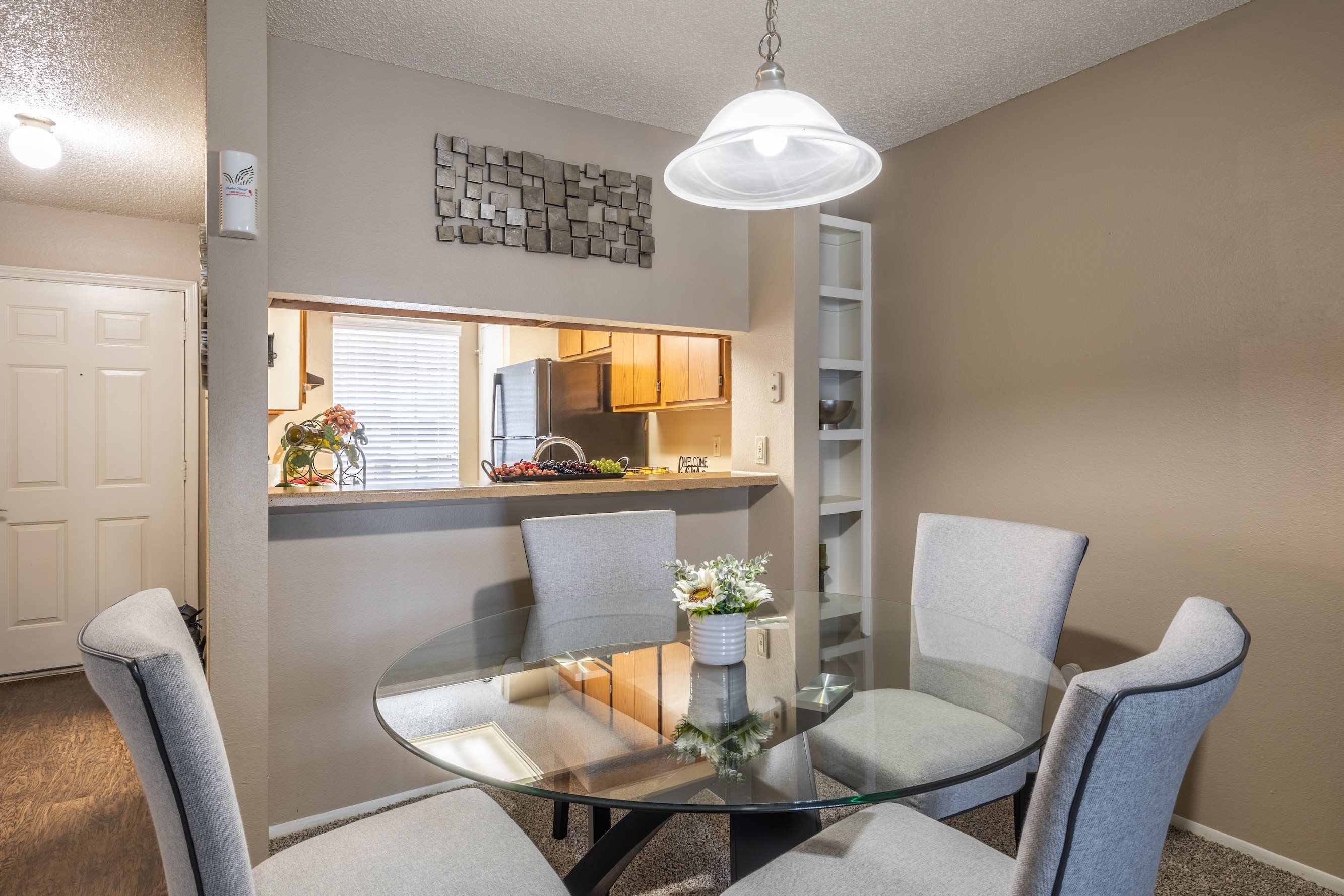 A dining room with a glass table and grey chairs.