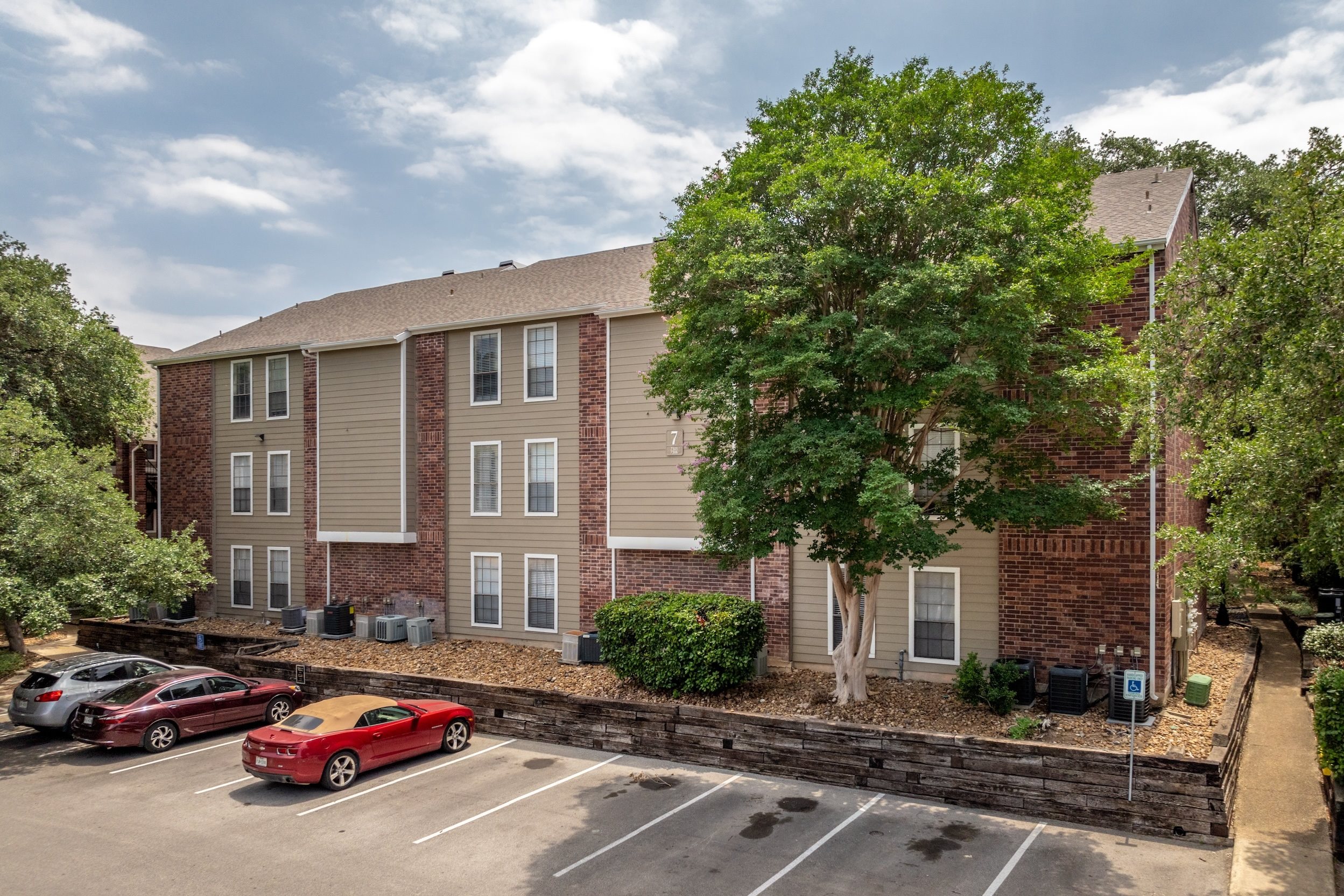 A red car is parked in a parking lot in front of a brick building.