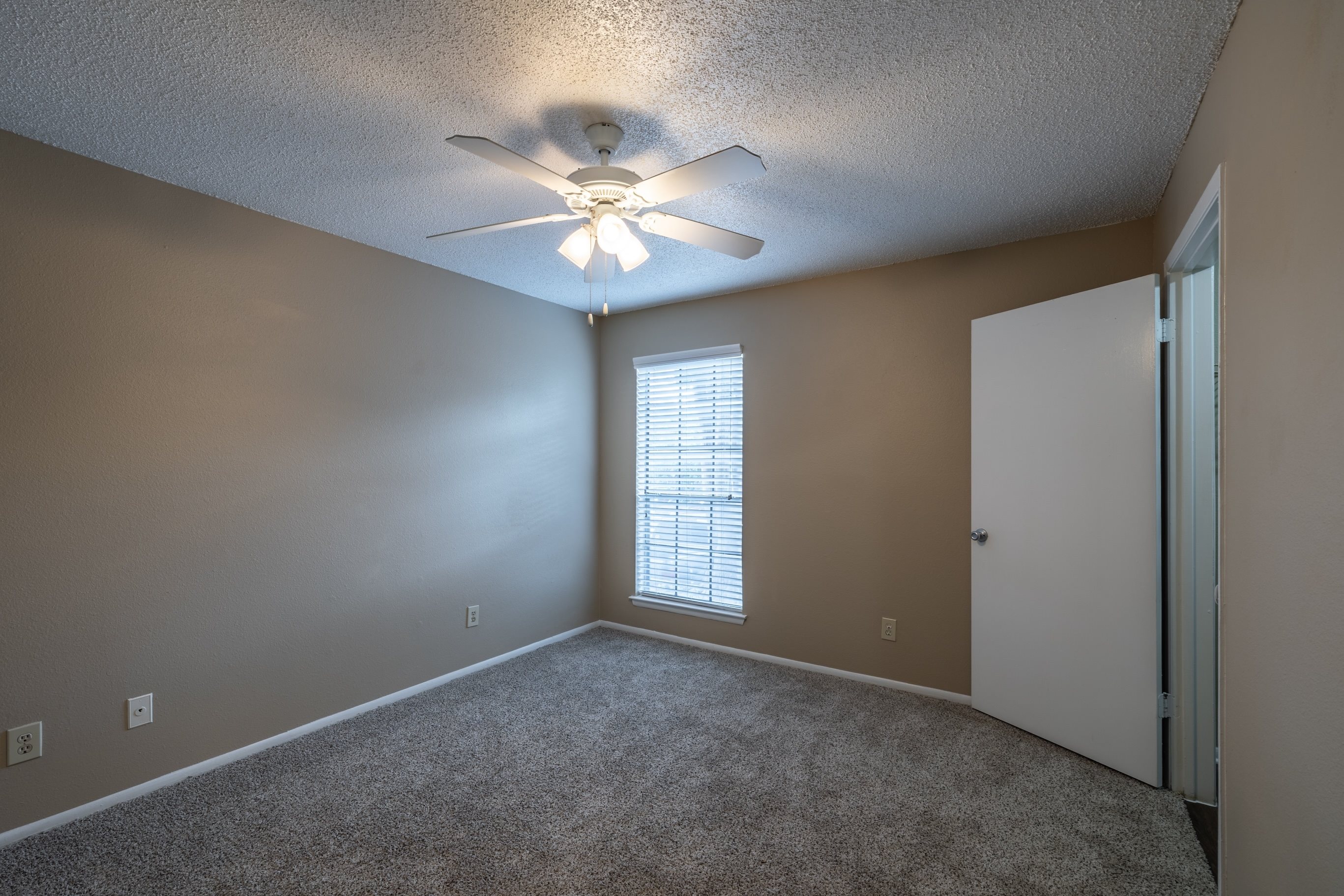 A room with a ceiling fan and a window with blinds.