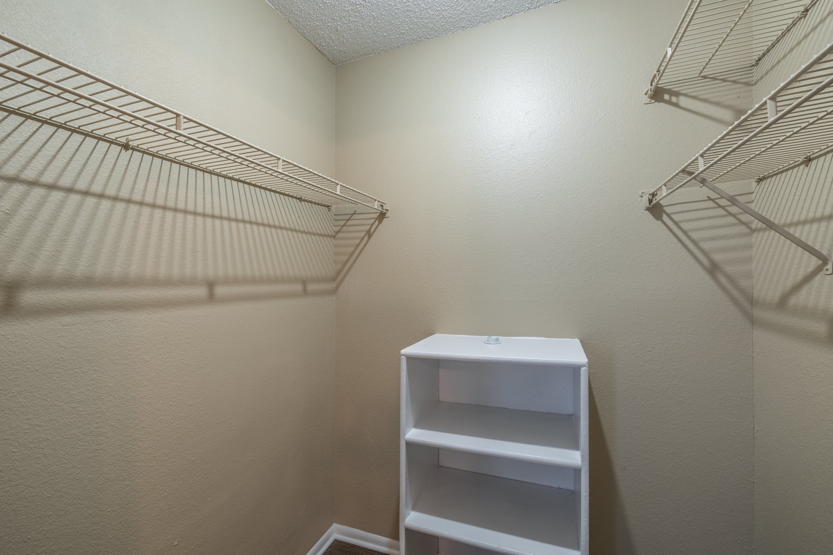 A white shelf unit with three shelves is in a room with white walls.
