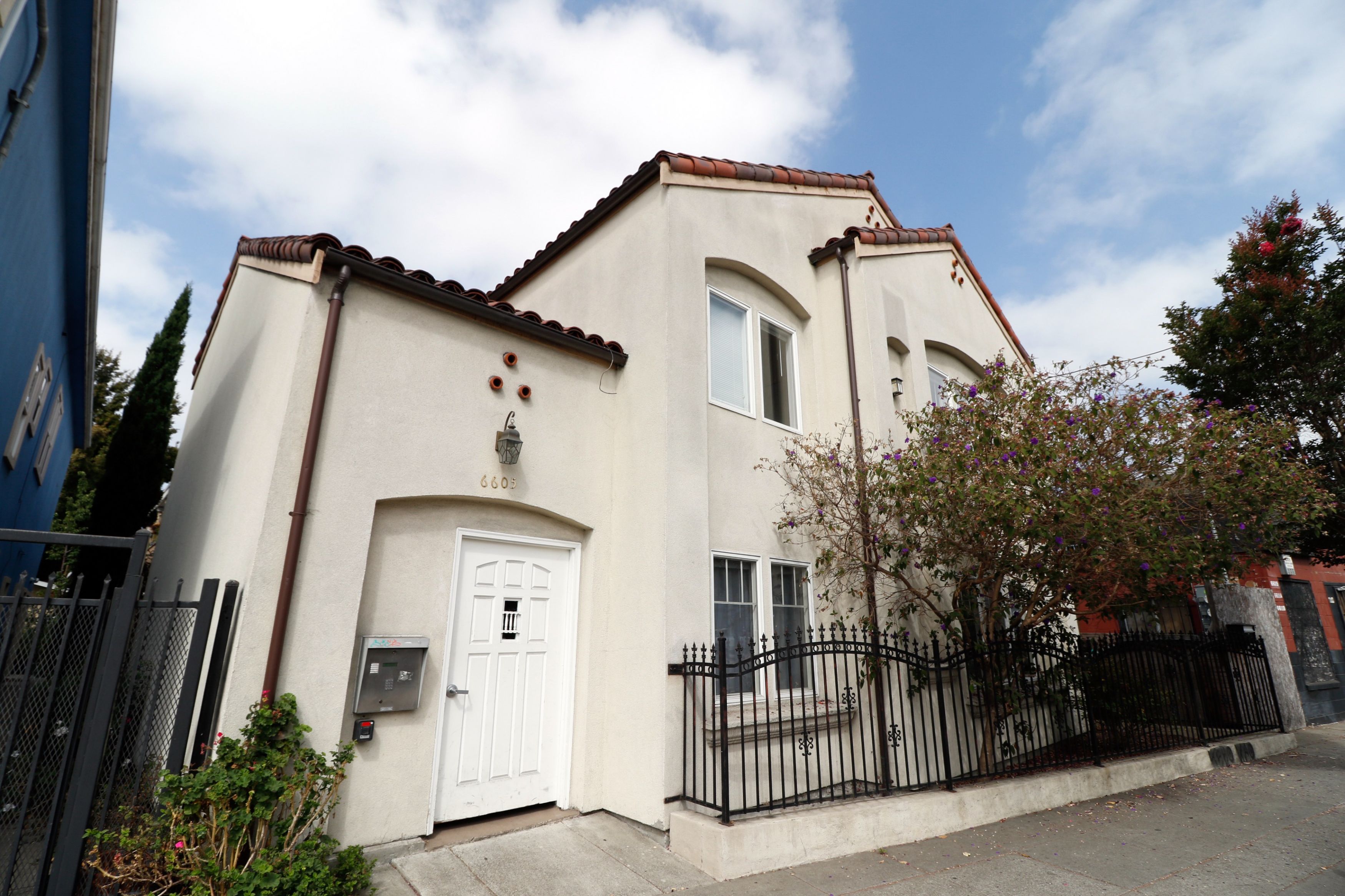 A white house with a black gate and a brown roof.