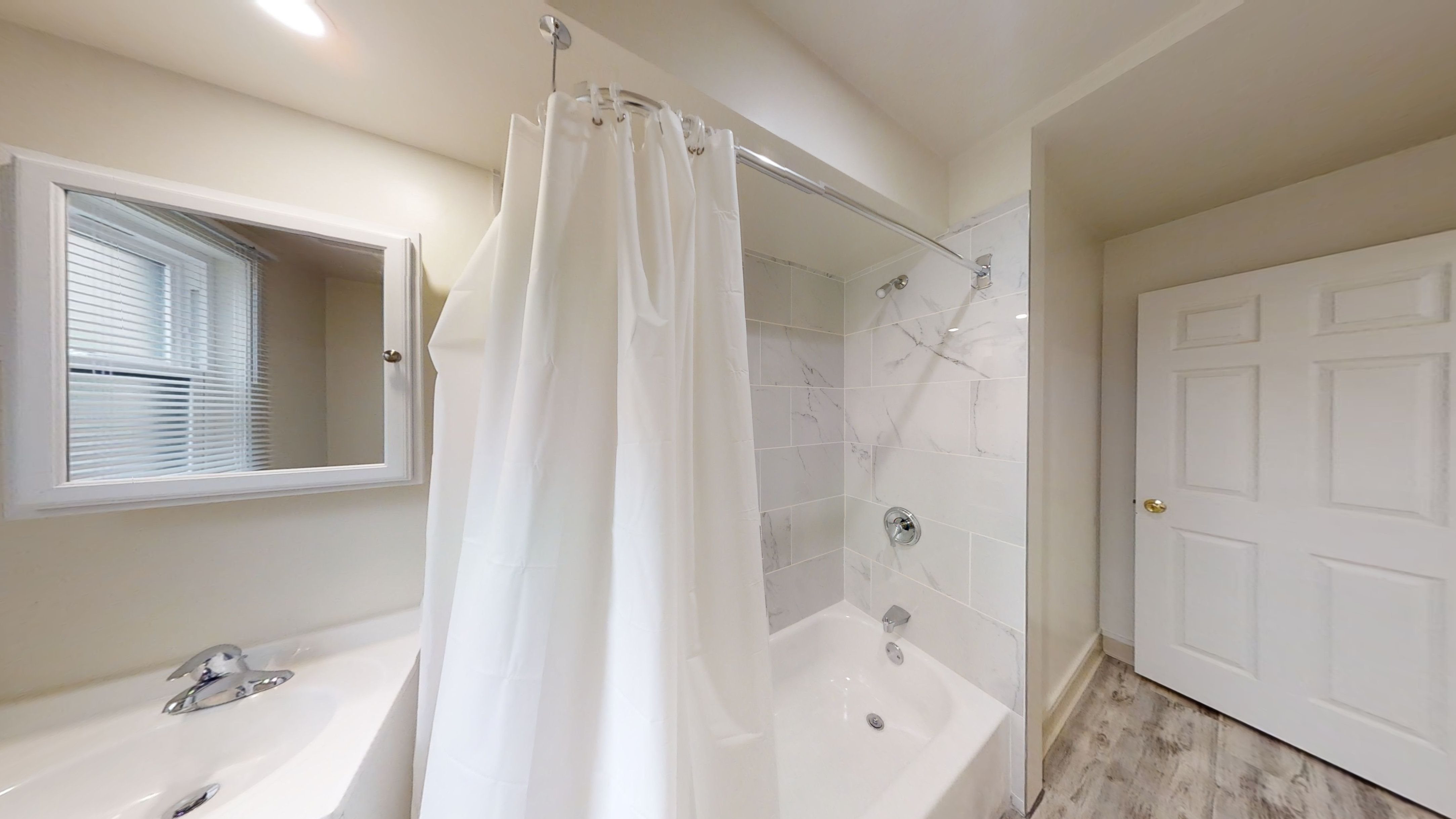 A white bathroom with a tub, shower, and a window.