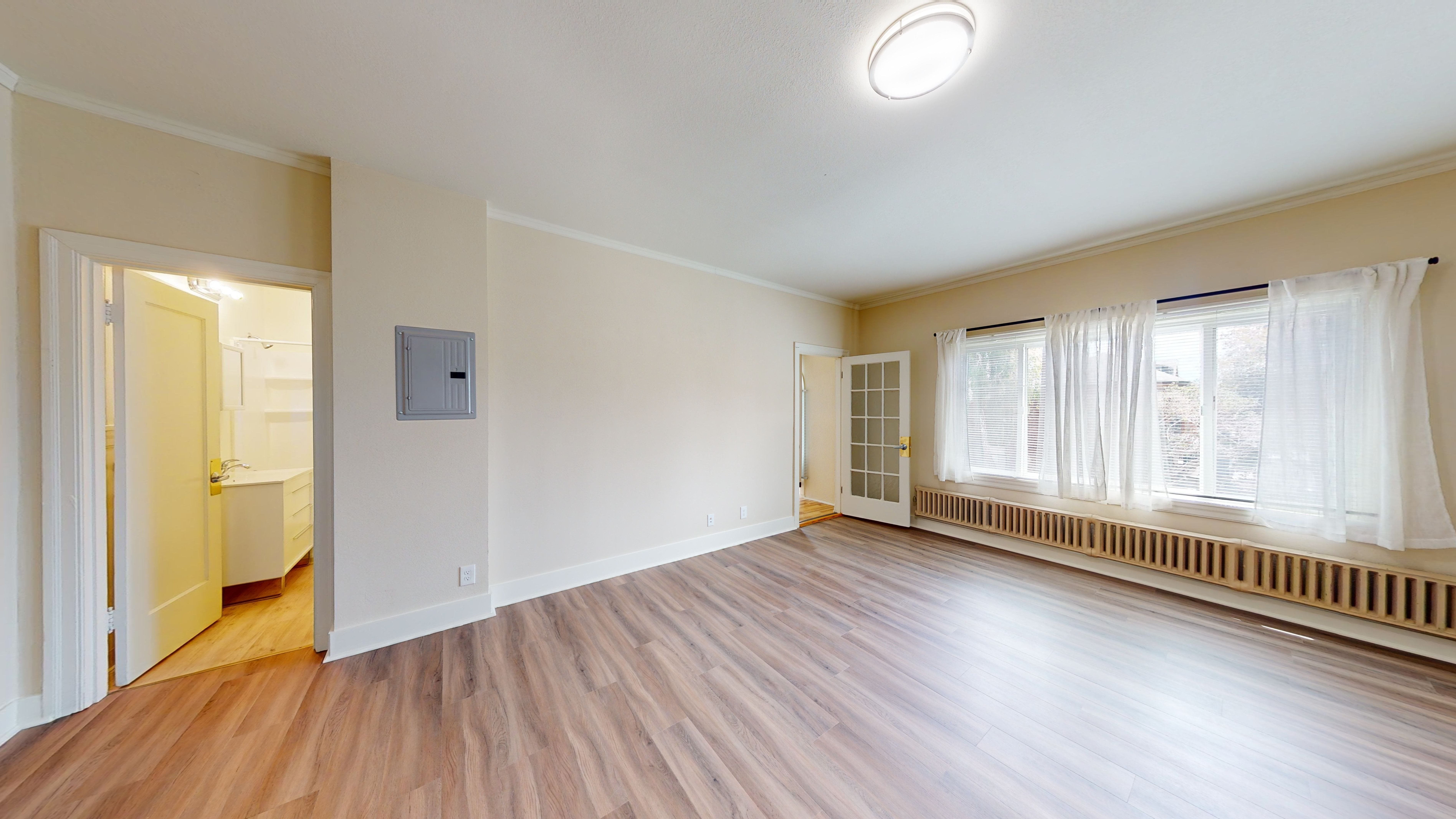 A room with wooden floors and a window with white curtains.