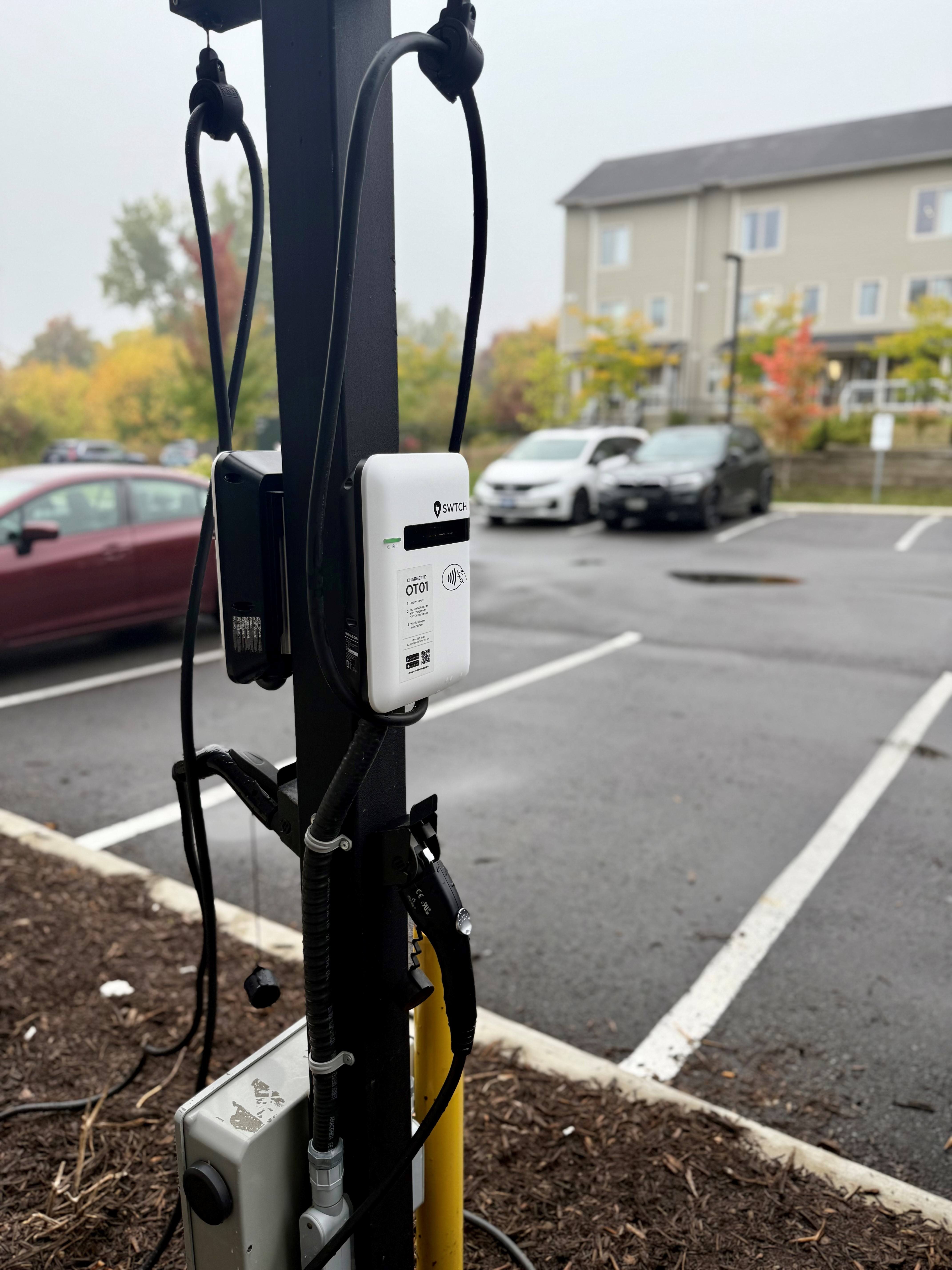 A charging station for electric vehicles is shown with a car in the background.
