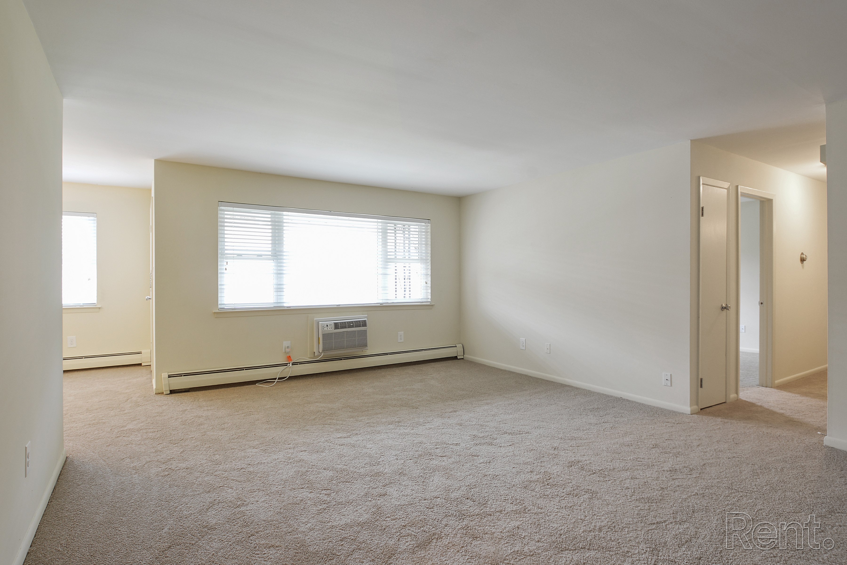 A large, empty room with a window and carpeted floor.
