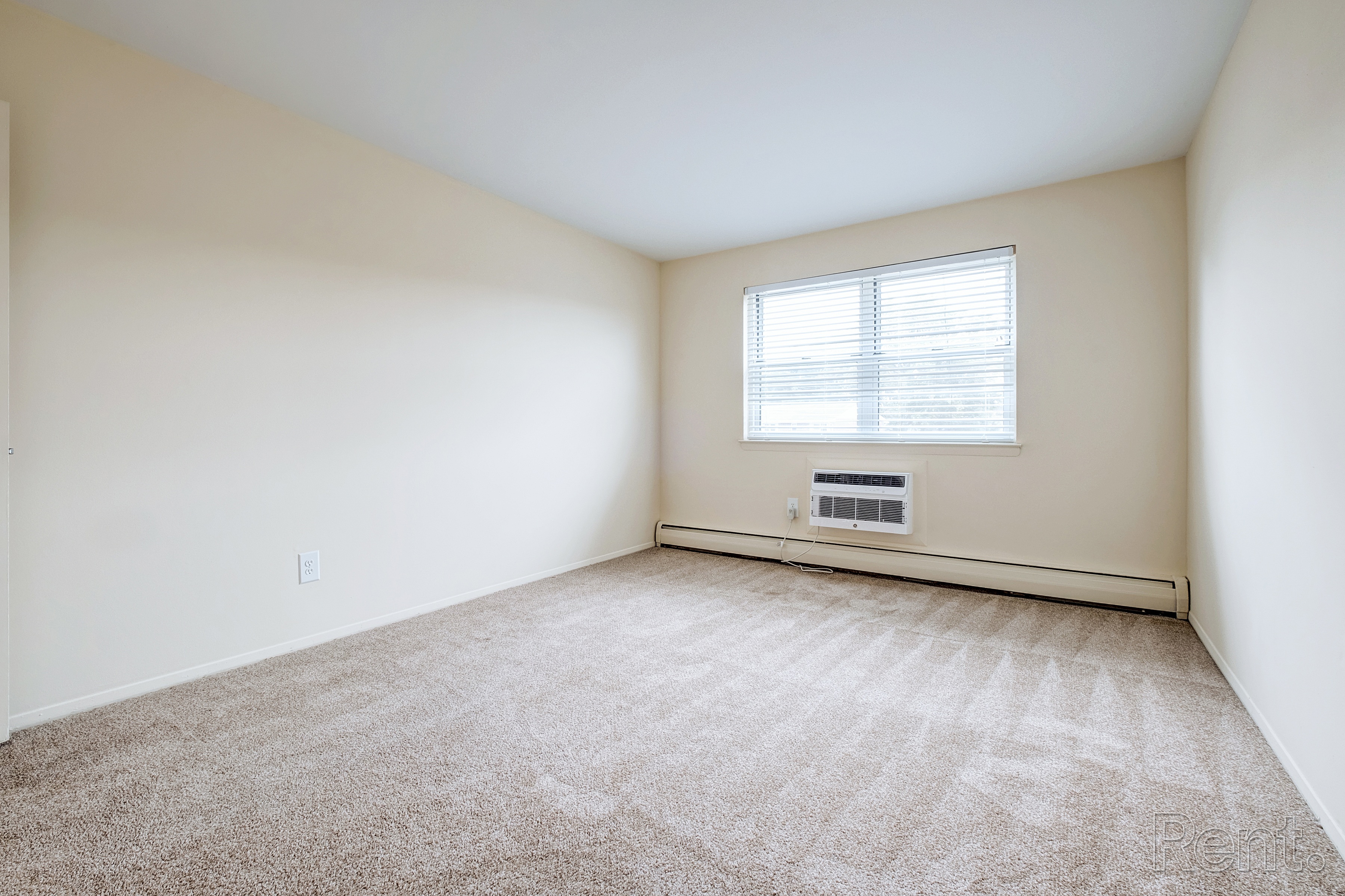 A room with a carpeted floor and a window with blinds.