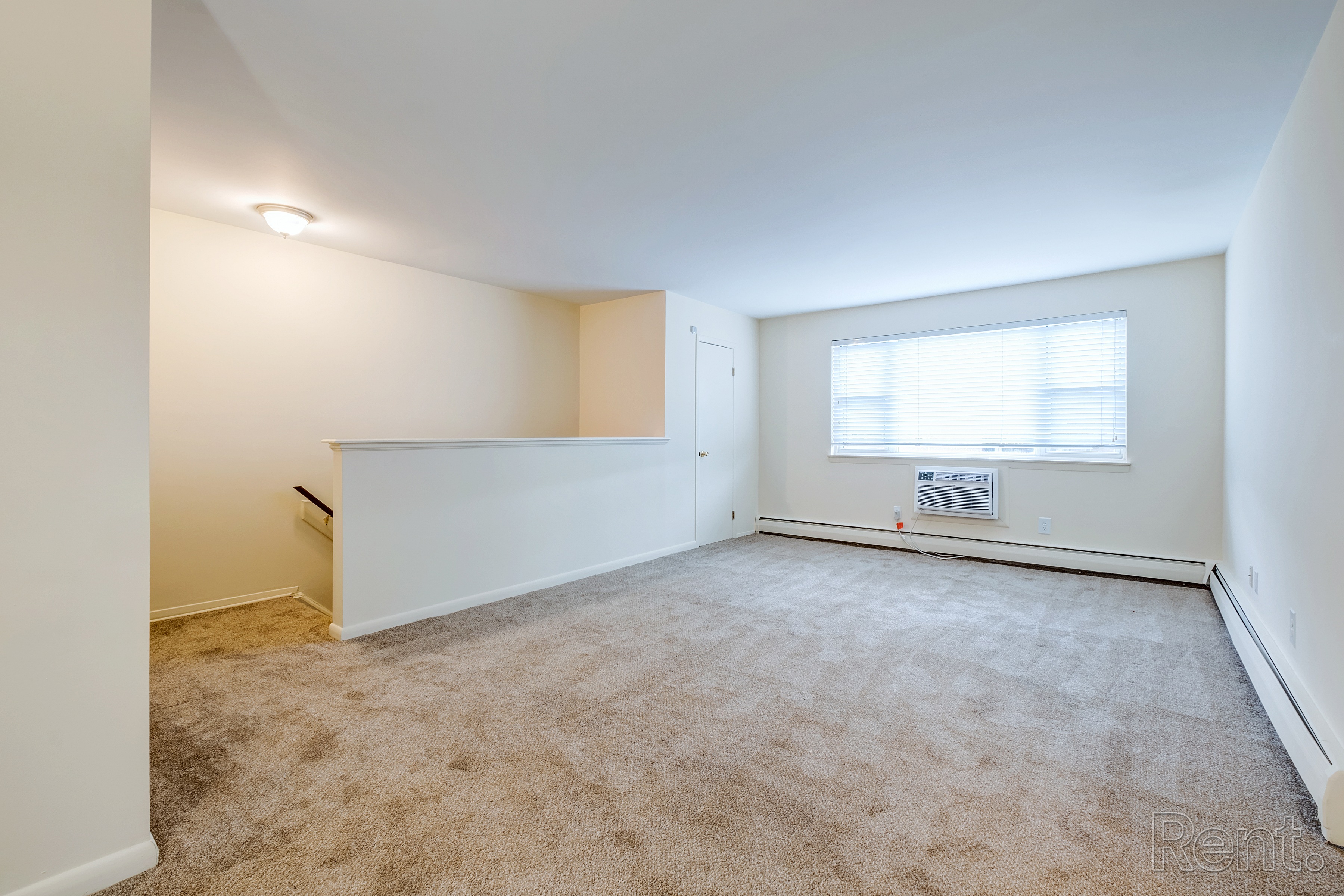 A large empty room with a carpeted floor and a window.