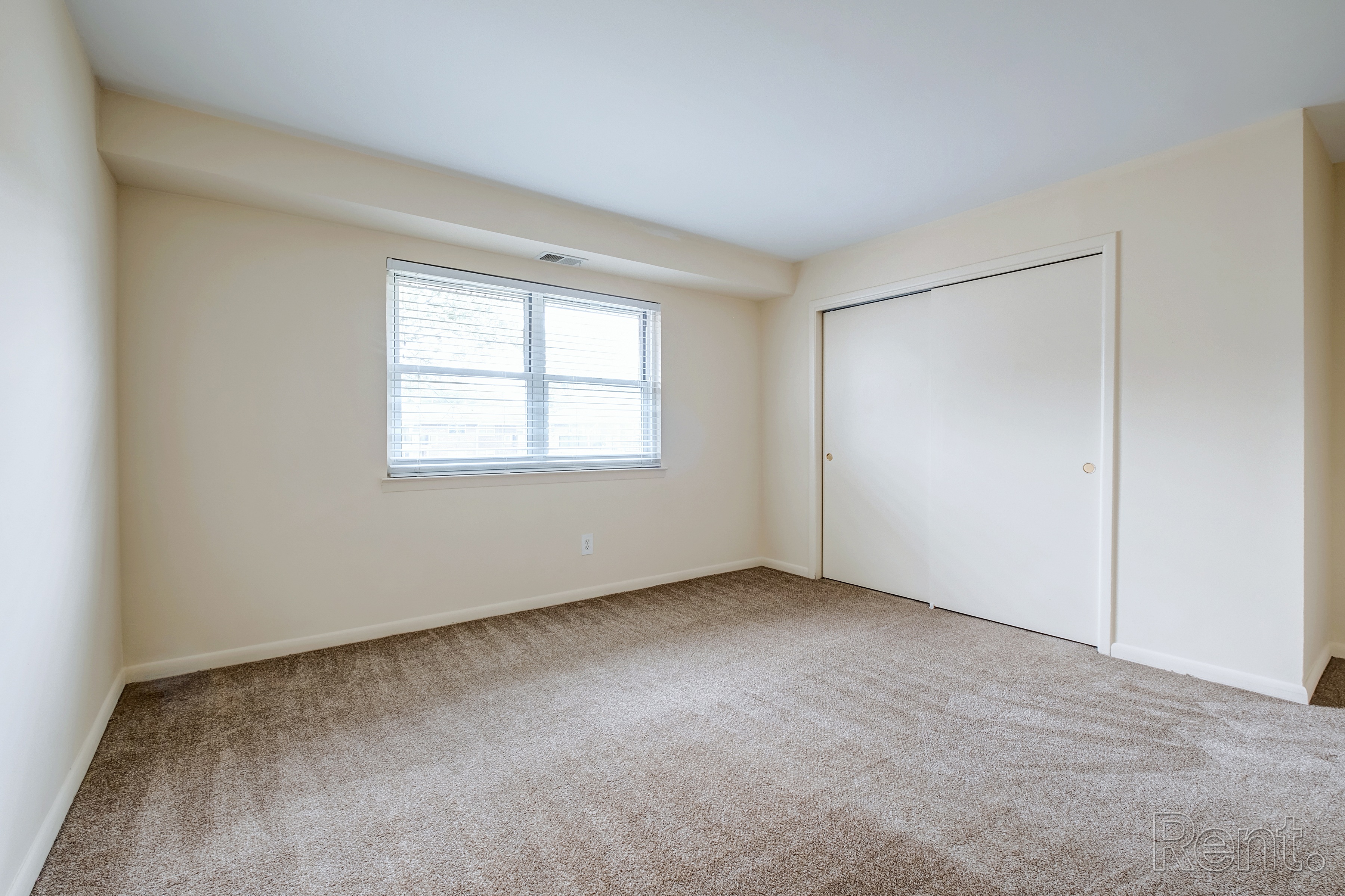 A room with a carpeted floor, a window, and a door.
