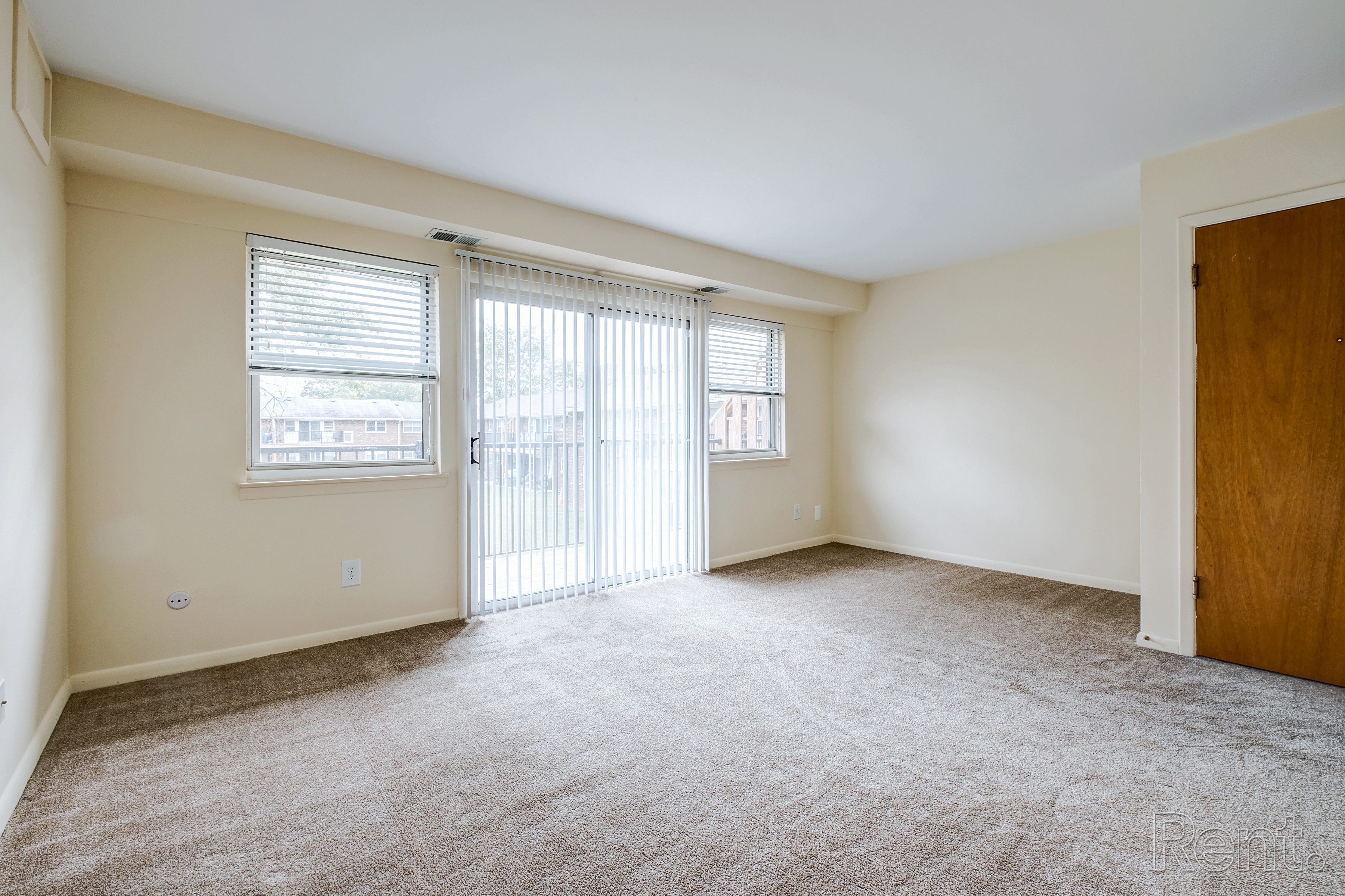 A room with a carpeted floor, a sliding glass door, and a wooden door.