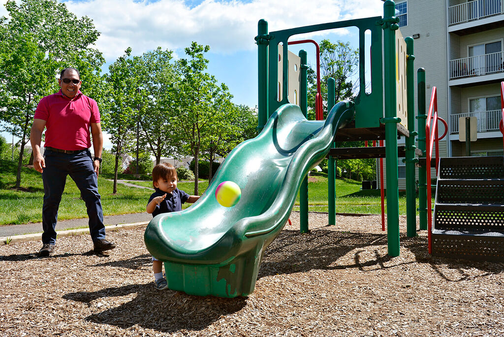 A child playing on a green slide with an adult standing nearby.