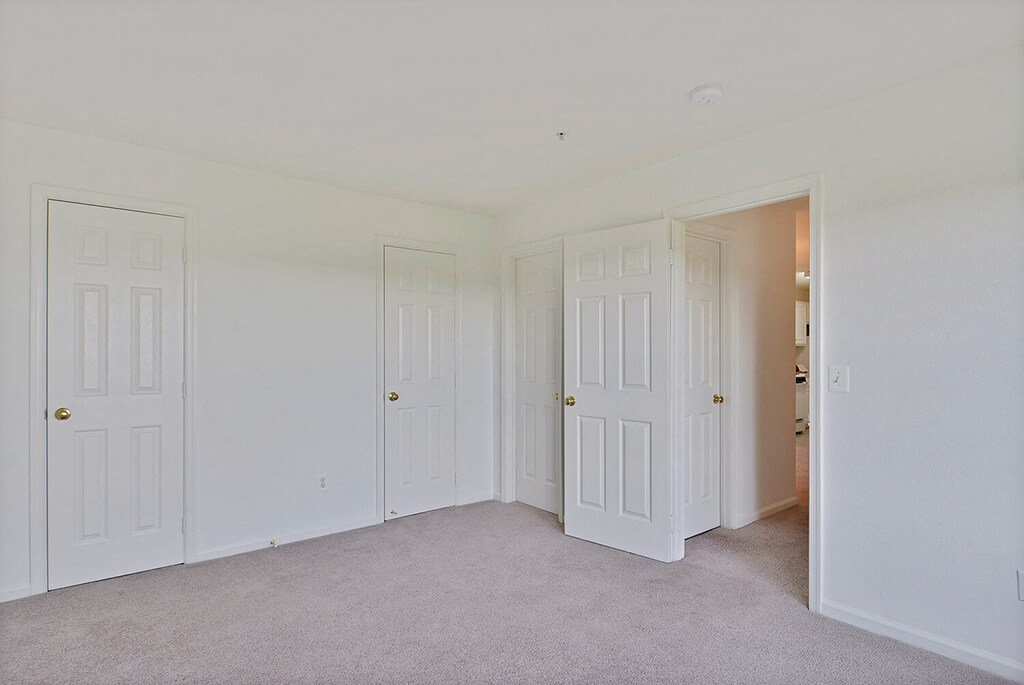 A room with white doors and carpeted floor.