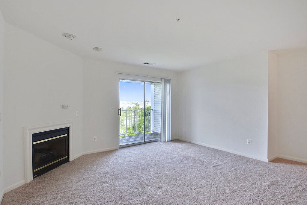 A large, empty room with a fireplace and sliding glass doors leading to a balcony.