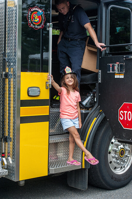 A little girl is standing on the step of a fire truck.