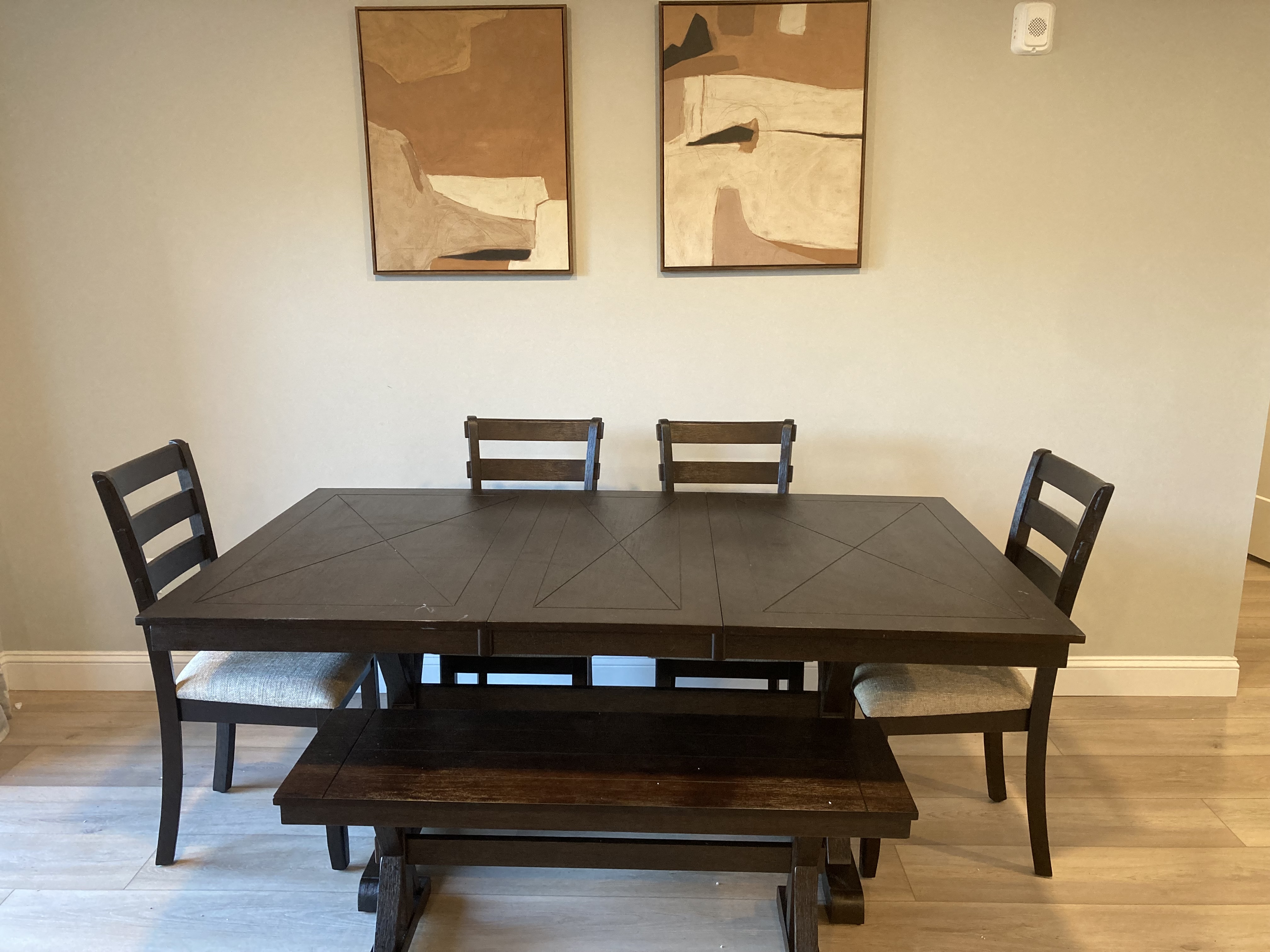 a dining room table with chairs and two paintings on the wall