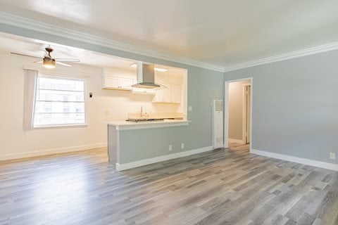 an empty living room with a kitchen and a window