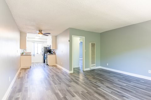 an empty living room and kitchen with wood floors and a ceiling fan