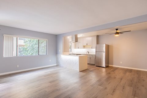 an empty living room with a kitchen and a large window