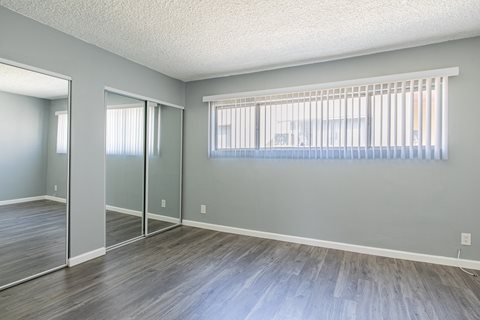 A room with grey walls and wooden flooring with a window covered by a white blind.