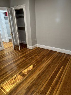 A room with a wooden floor and a door open to another room.
