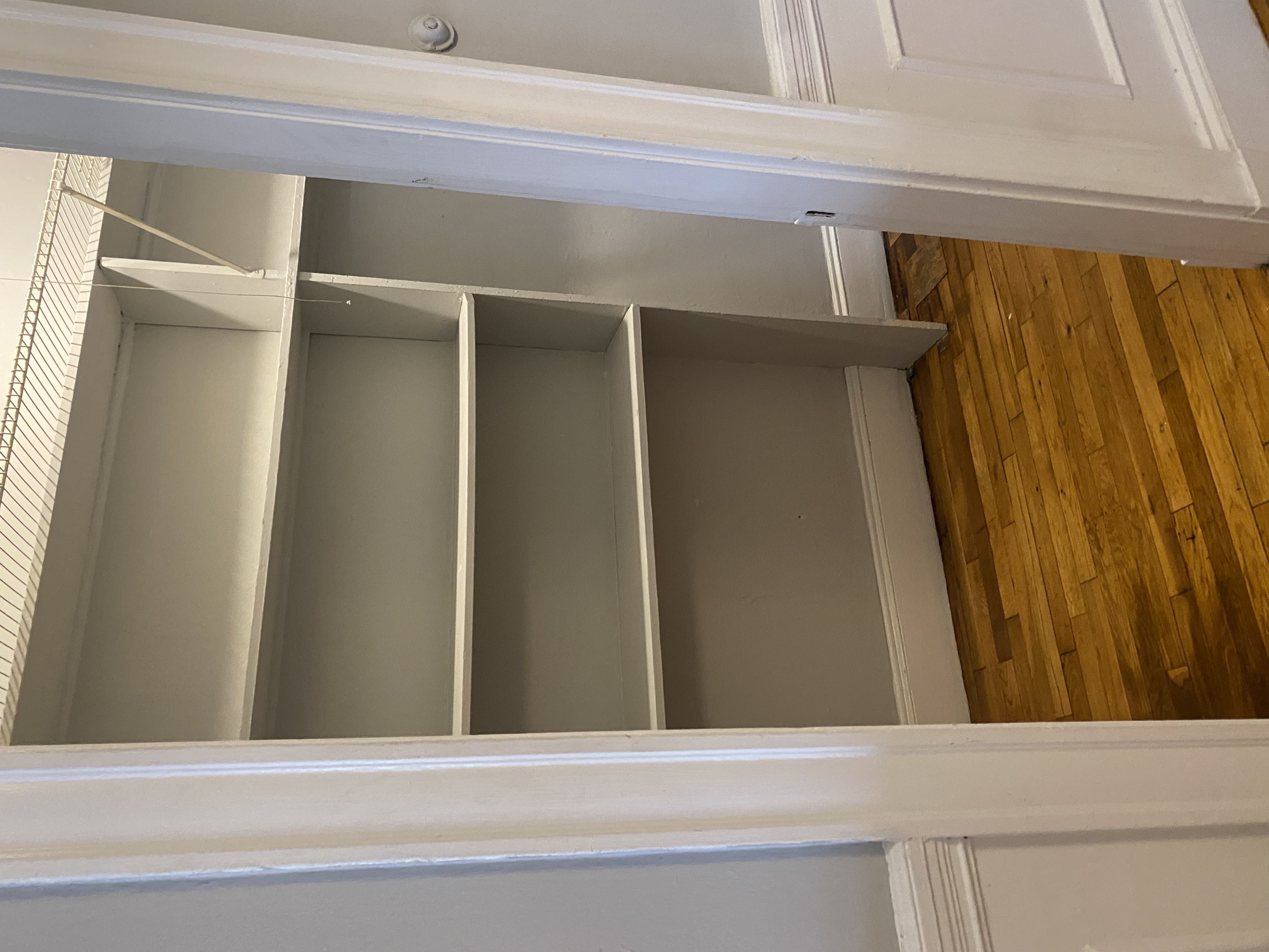 A white shelf with four glass panes is mounted on a white wall.