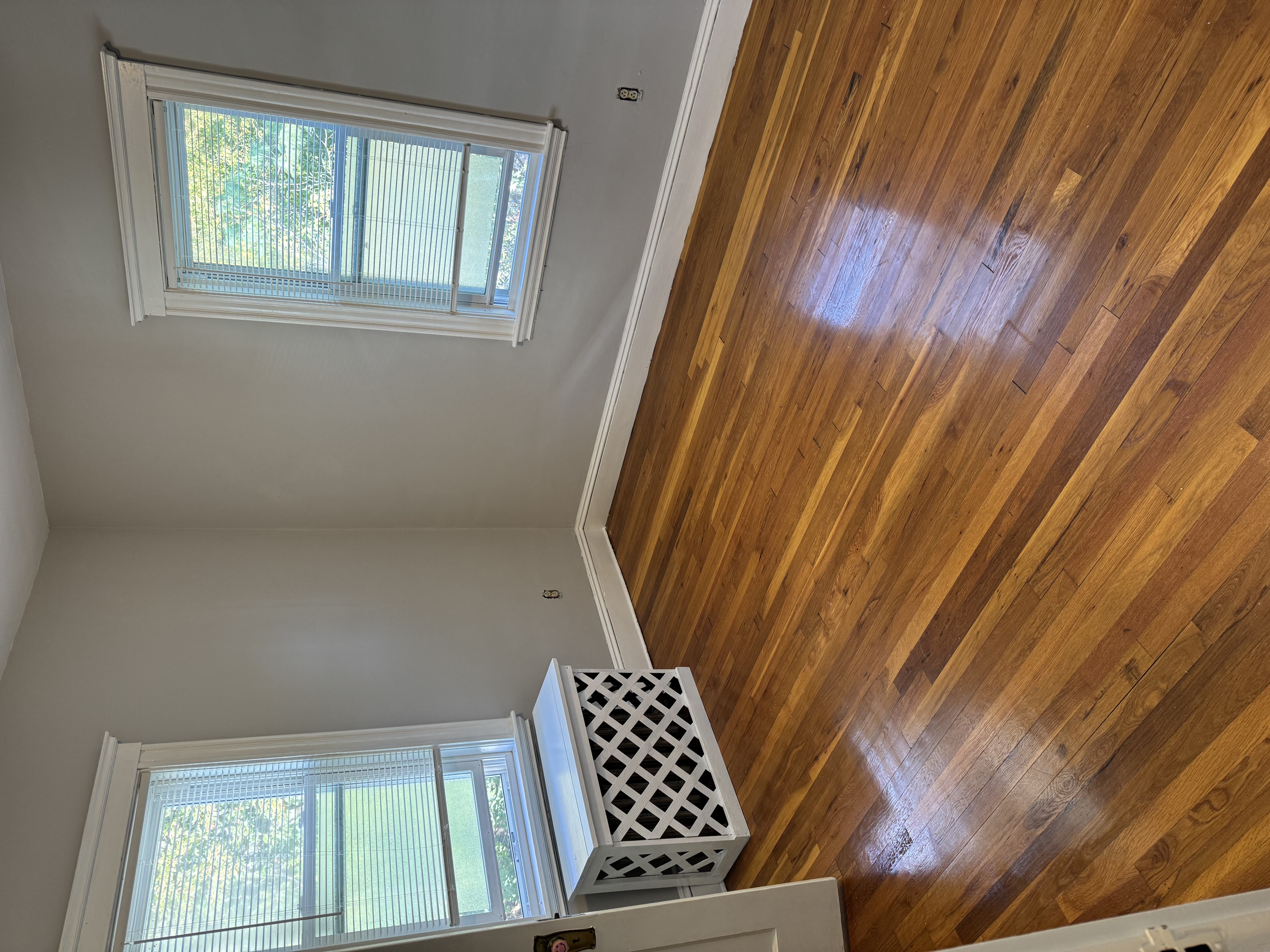 A white air vent is on the floor next to a window.