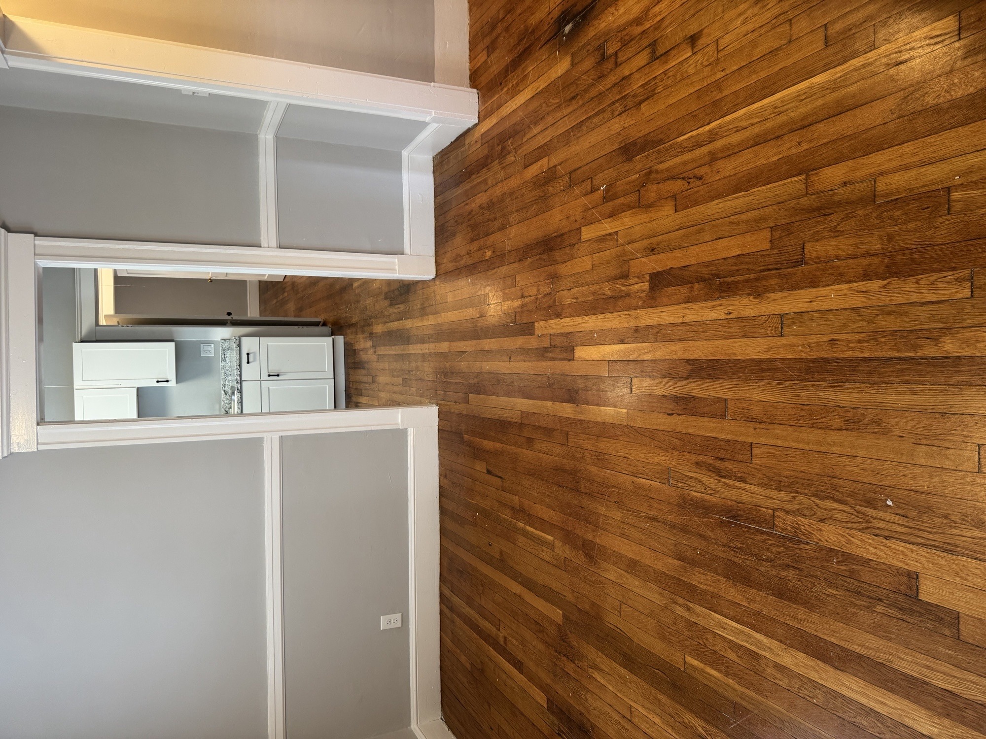 A white refrigerator is in a kitchen with a wooden wall.